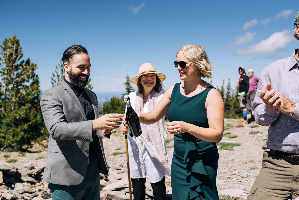 Elopement wedding guests pouring champagne on mountain summit