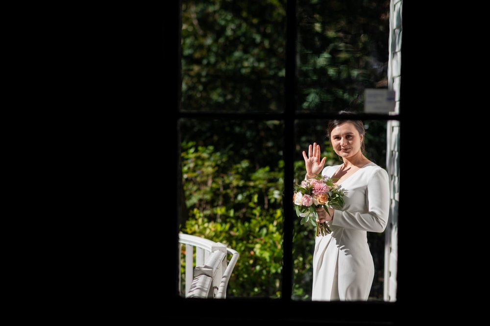 Candid of bride through window waiving to Photographer