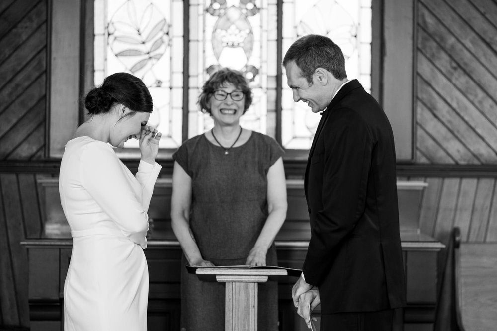 Candid black and white moment of bride and groom laughing during ceremony