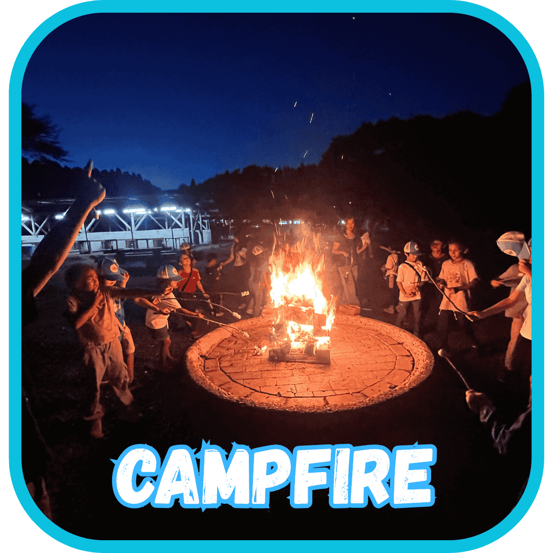 英語サマーキャンプでキャンプファイヤーを囲み、マシュマロを焼いたり踊ったりする子供たち