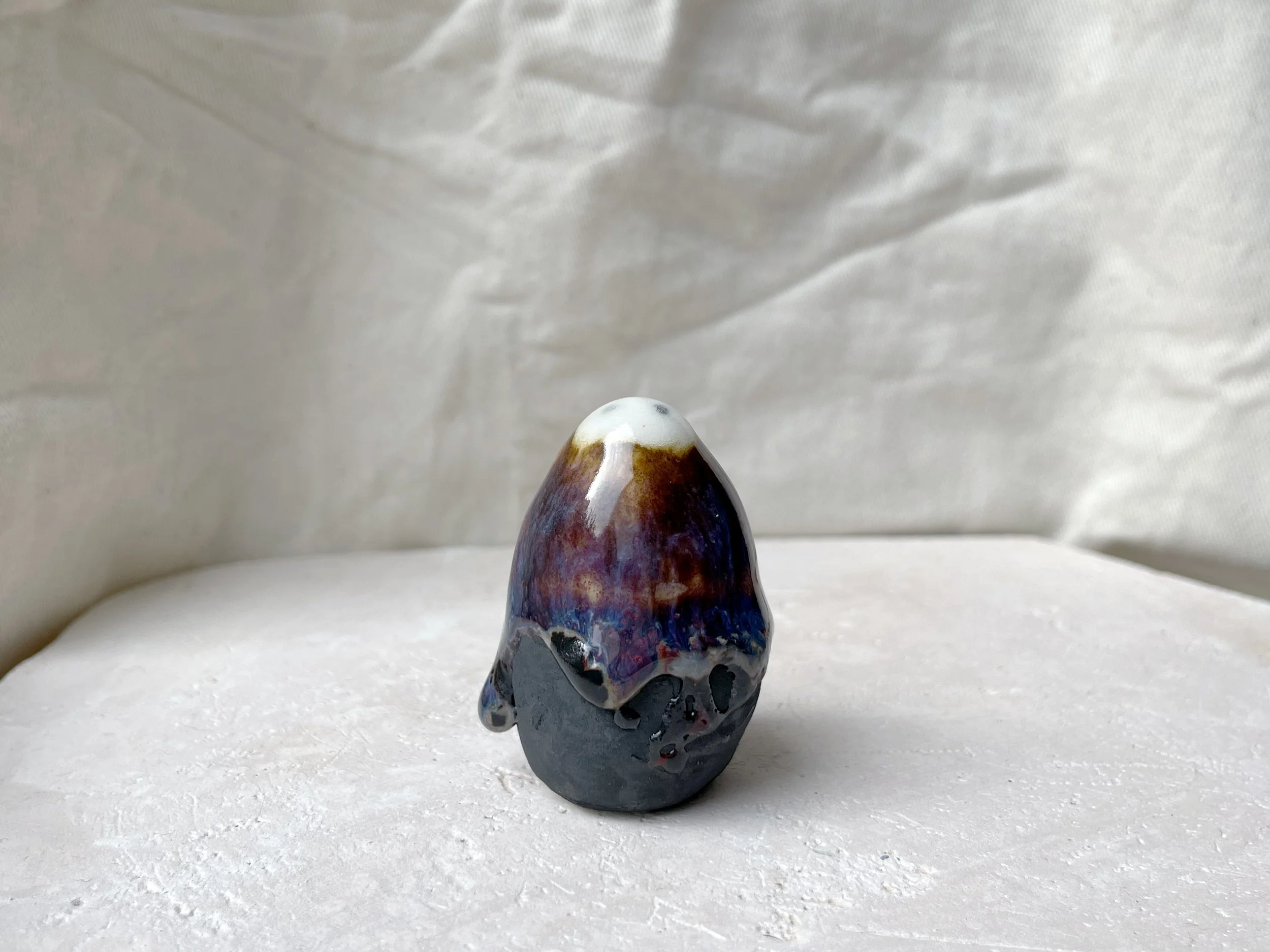 Brown, purple, blue and black handmade figurative ceramic sculpture with glossy runny floating glaze