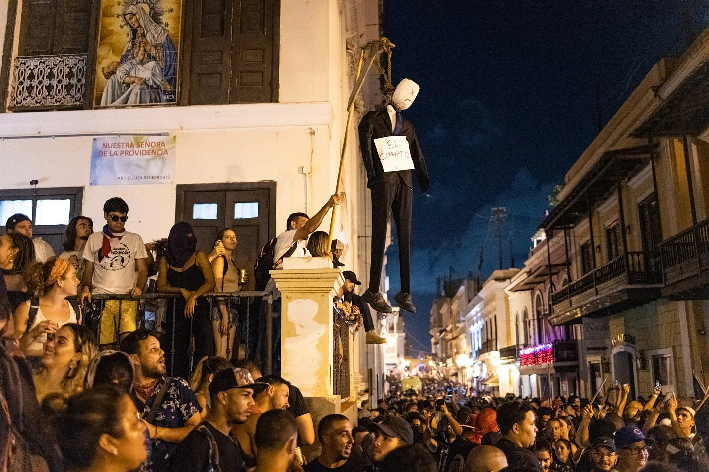  A demonstrator holds a dummy being hung in a suit with a sign around its neck that reads "El Corrupto" among the massive crowd that leads down to the Governor's mansion the night Governor Ricardo Rosselló announced his resignation. San Juan, Puerto 