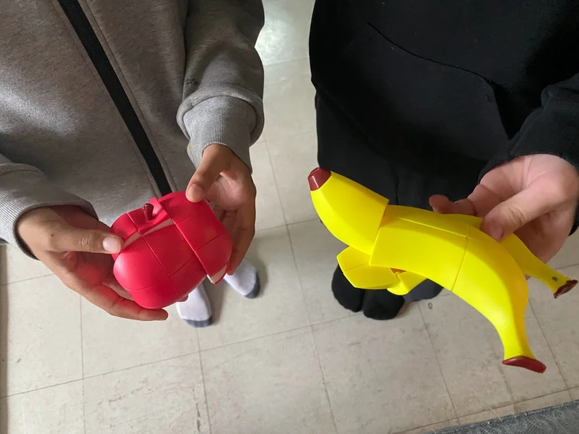 two young people's hands, holding Rubix fruit - a scrambled apple and banana