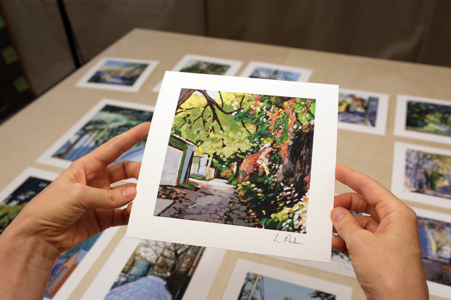 Leslie Parker holding a fine art print of a leaf-covered Leslieville laneway fence
