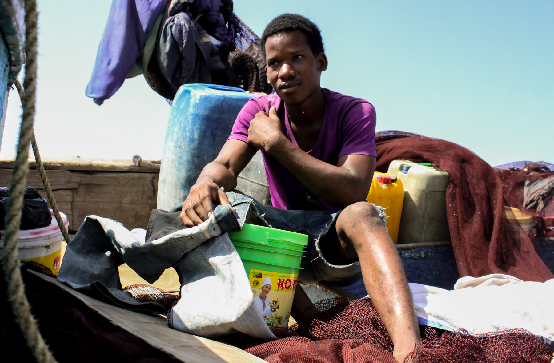 A young fisherman repairs his jeans while waiting for the tide to return in Bagamoyo, Tanzania