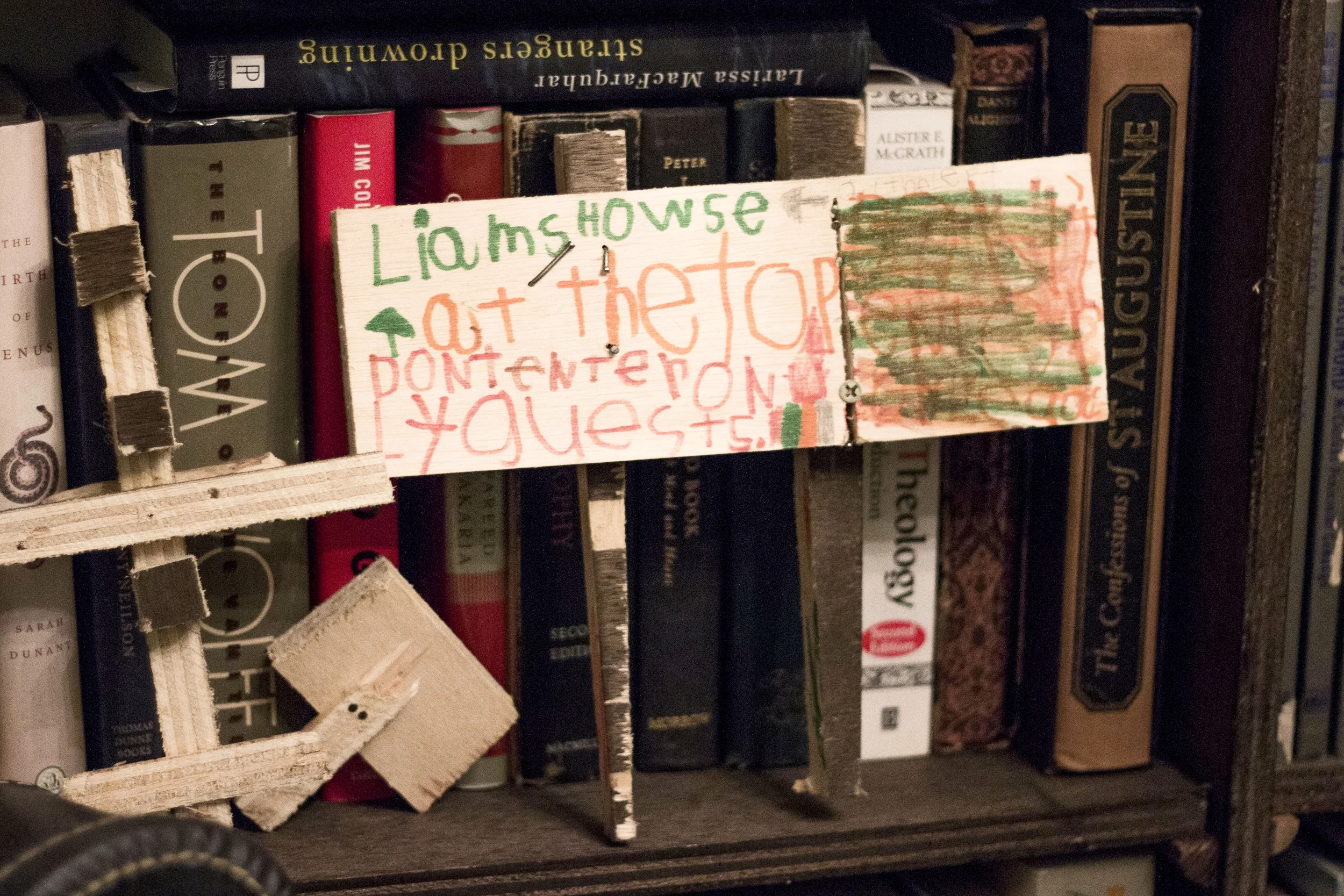 Liam’s sign, which reads “Liam’s howse at the top don’t enter only guests,” rests on Kiranne’s bookshelf. The bookshelf occupies almost an entire wall of their apartment. 