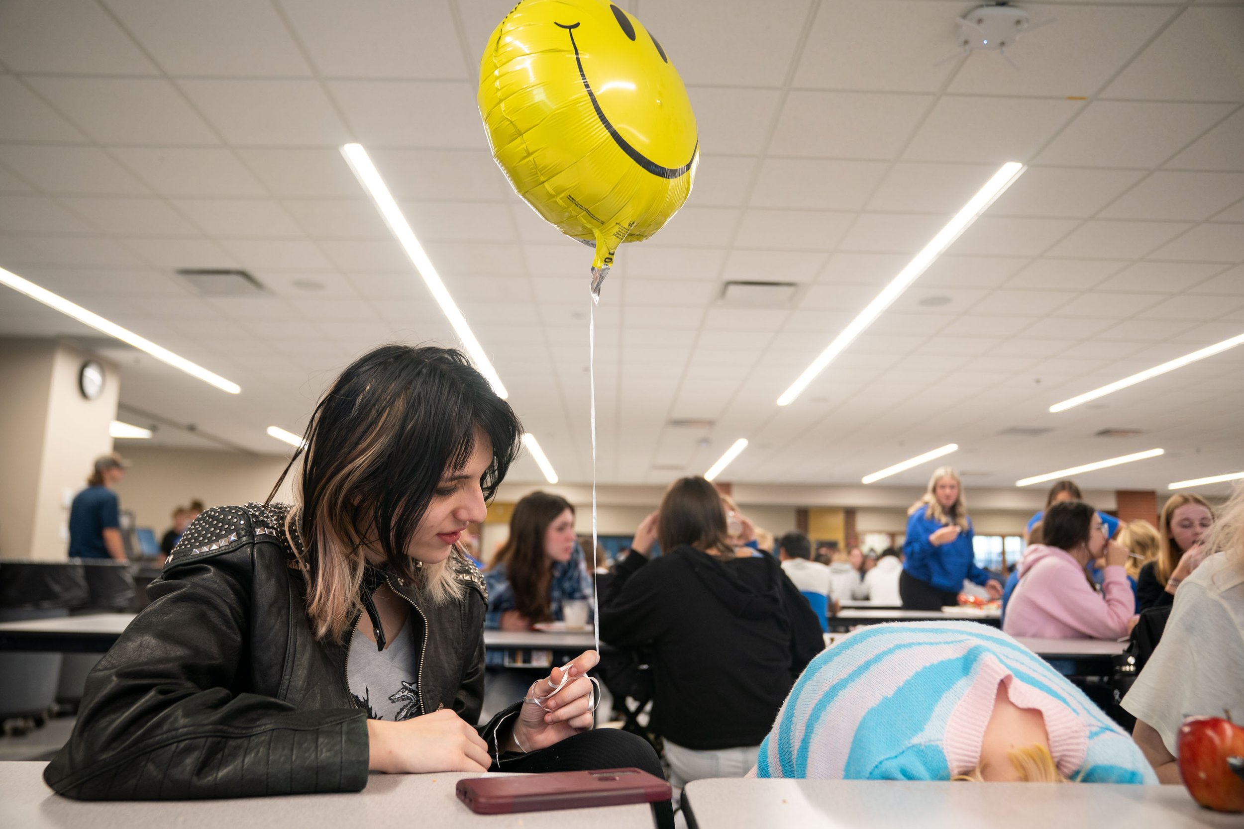  Irie Nordstrom, 15, holds a smiley face balloon while Lily Nickel, 15, retreats under the cafeteria table during their lunch break after a pep fest, a gathering of students to encourage school support typically before a sports event, at Brainerd Hig