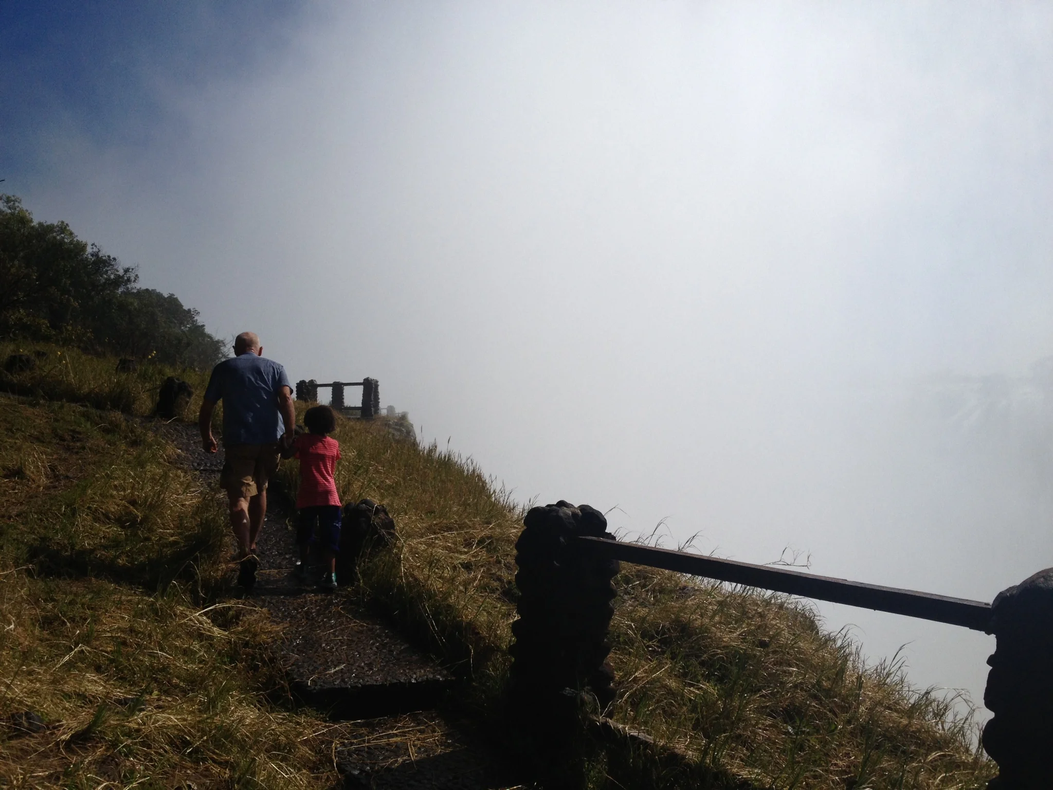  Man and child walking the mountain-side path overlooking Victoria Falls. 
