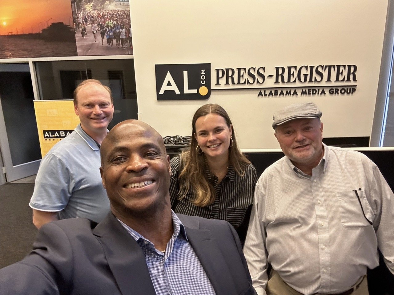 Hollis Towns and three others smiling and posing for a picture at the Alabama Media Group office, in front of a "Press-Register" sign.