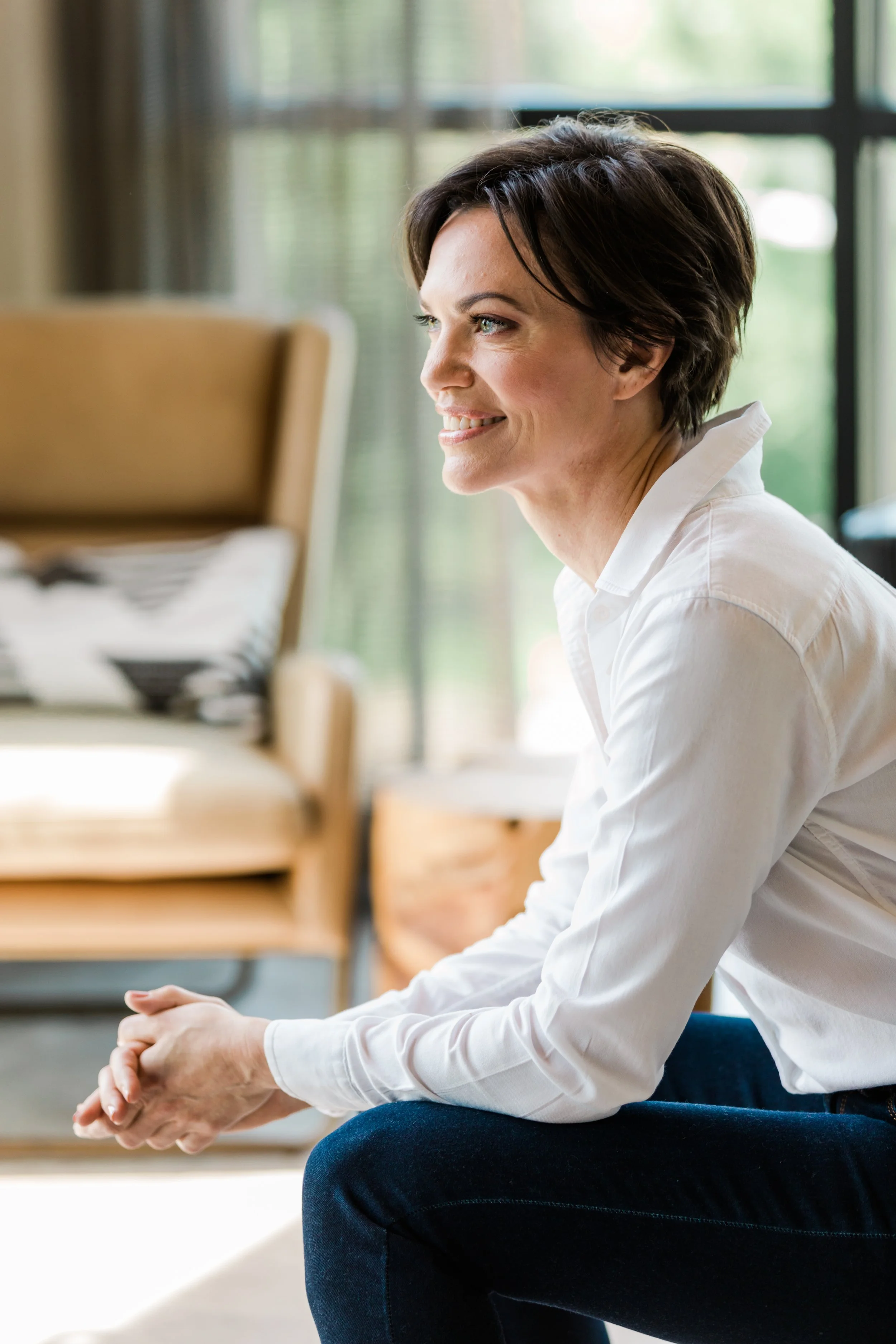 Heather Rees - woman sitting on couch, profile view, hands clasped