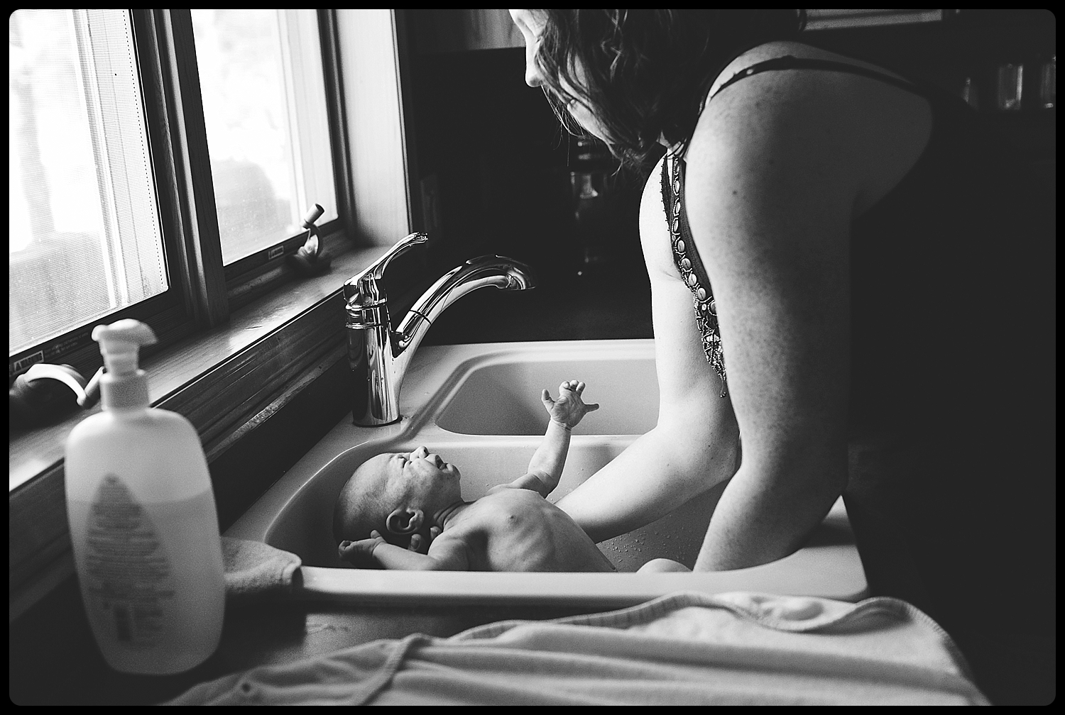 Mother gives newborn baby a bath in kitchen sink.