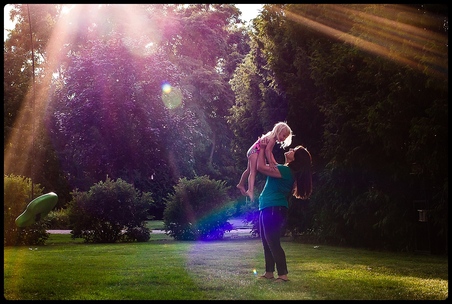 Mom holds daughter up into sun rays.
