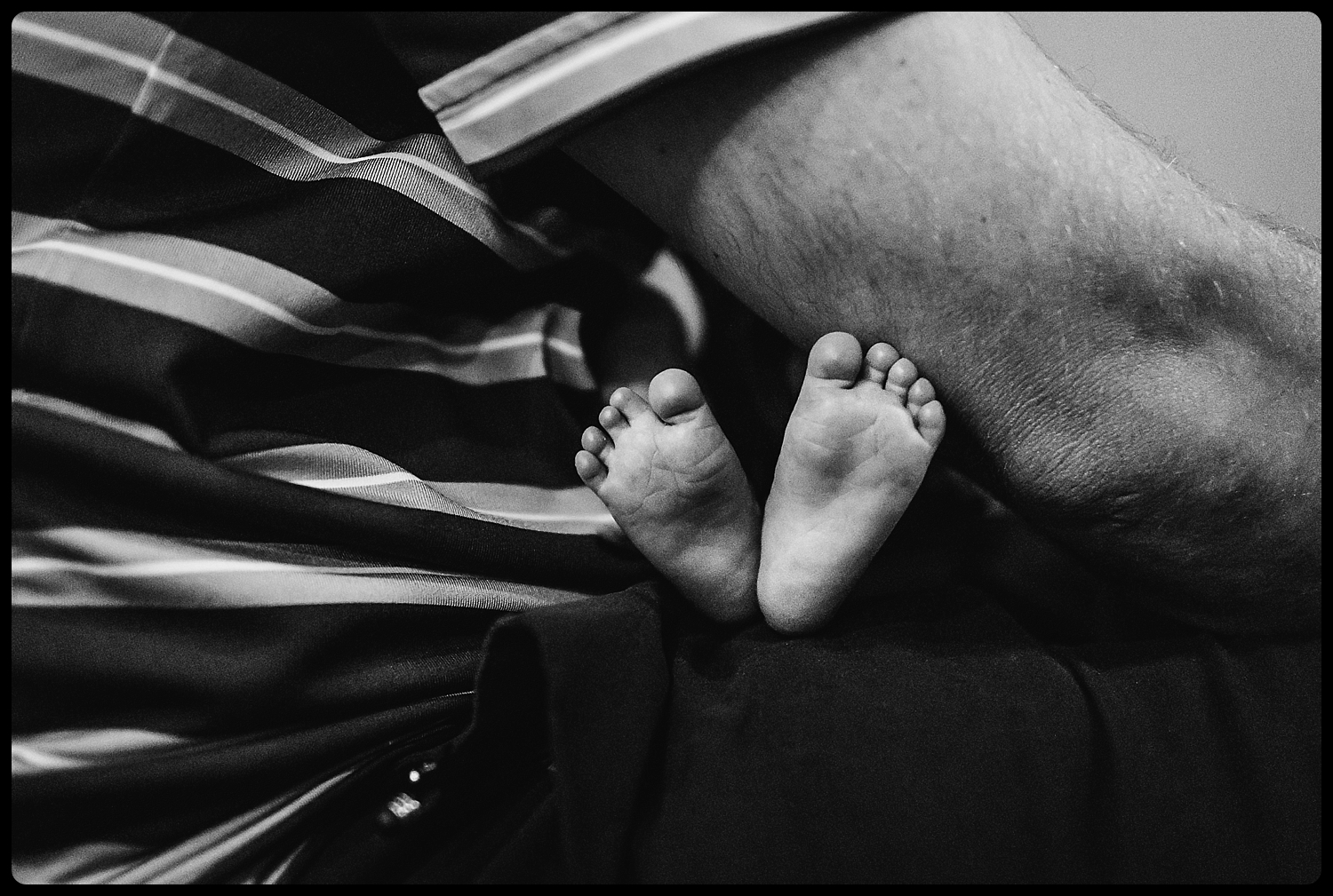 Father holds baby while his feet stick out from under his arm.