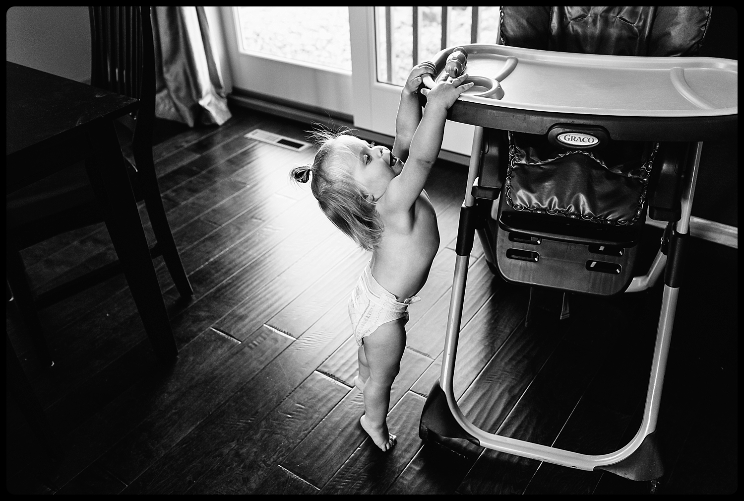 Toddler tries to reach the top of a high chair.