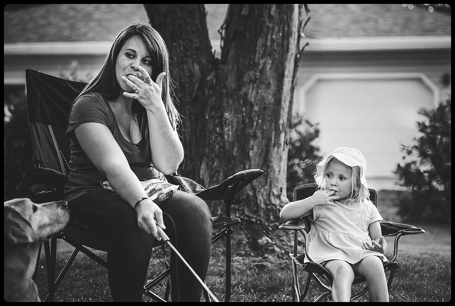 Mom and daughter both lick marshmallow from fingers at family bonfire.