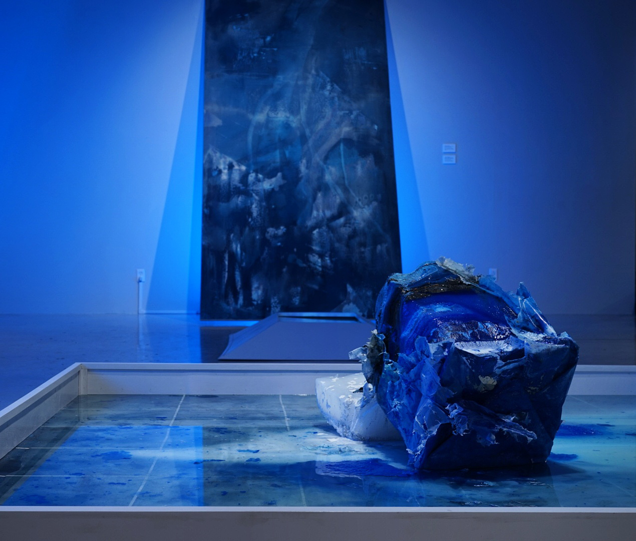 Like a glacier: An unpredictable portent not on your map. Ice embedded with acrylic, pigment, carbon, calcium carbonate, various materials. Cyanotype on cotton canvas. Lumber and spray paint. 82 inches x 82 inches x variable dimensions. 2017.
