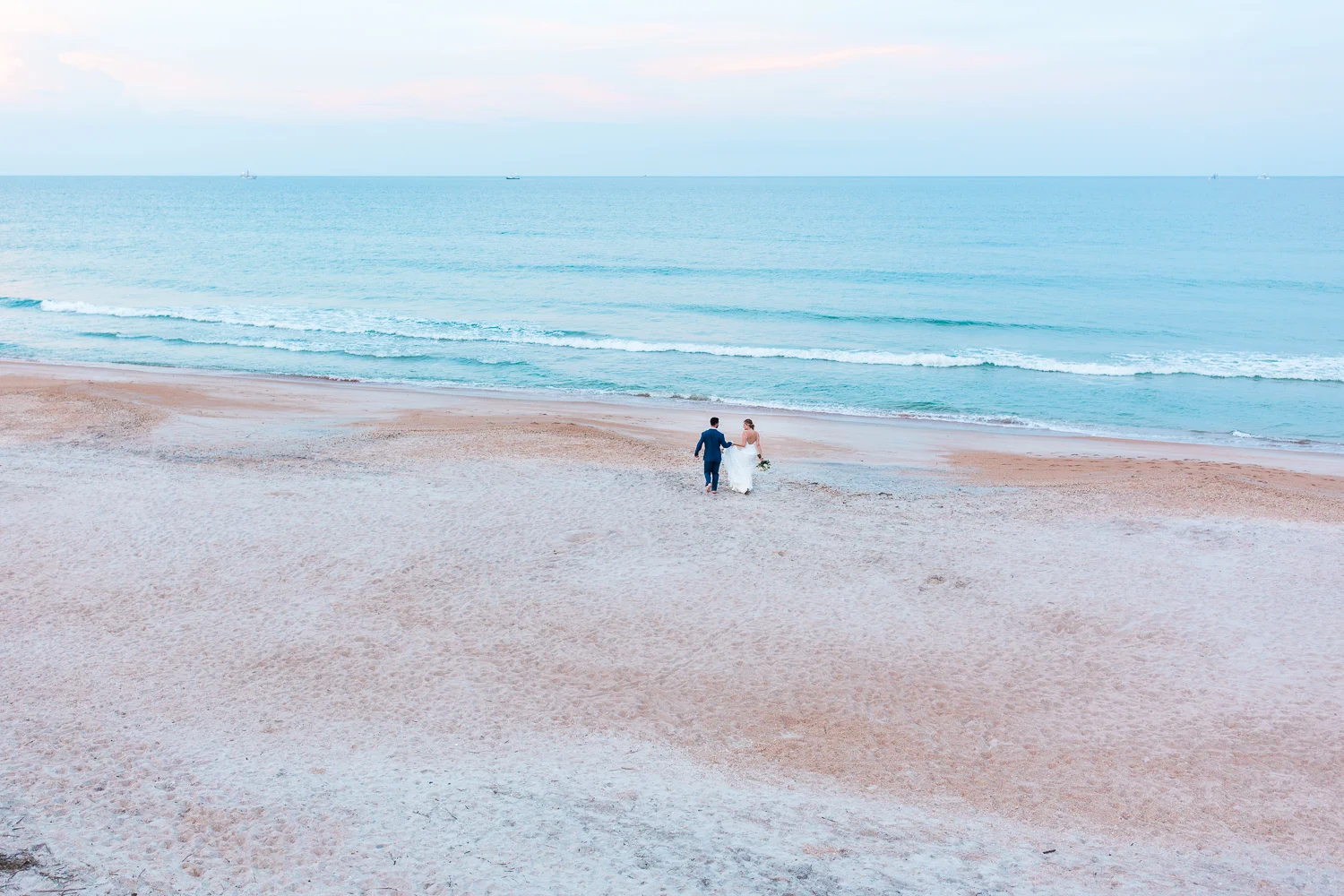 Stunning sunset picture of bride and groom running to the beach in Serenata Beach Club wedding