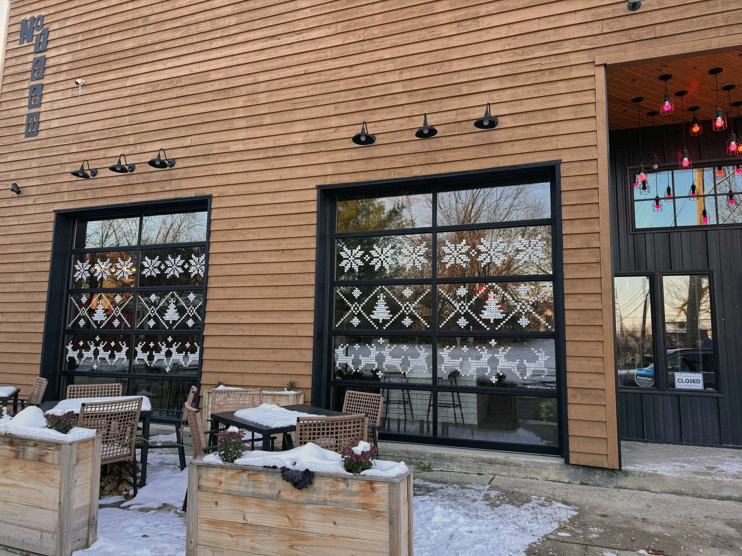 Exterior of a restaurant with snow-covered outdoor seating, large windows decorated with snowflake window decals, and a sign indicating it is closed.
