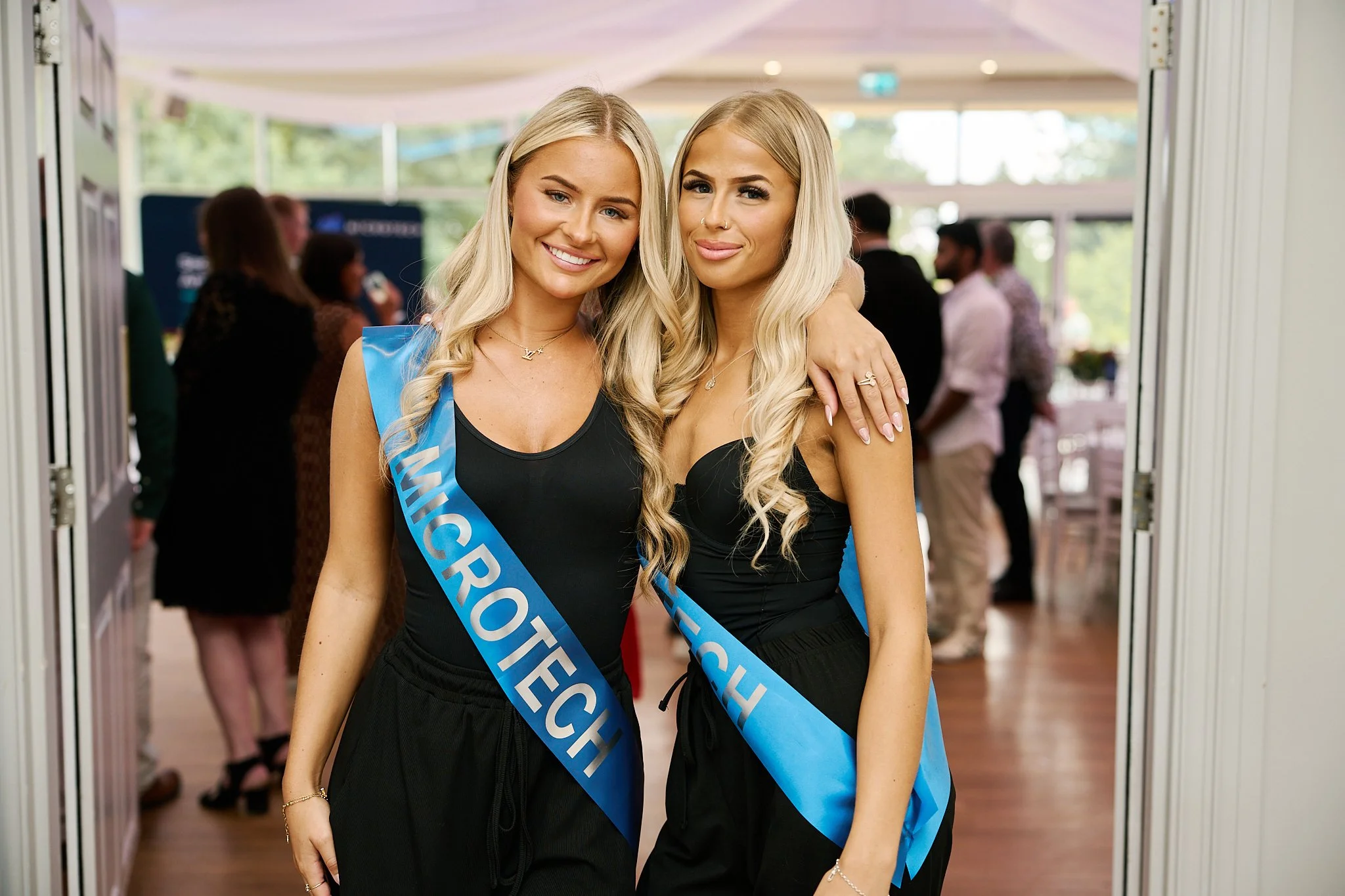 Two women wearing Microtech branded sashes at the company’s 40th anniversary celebration at Winstanley House