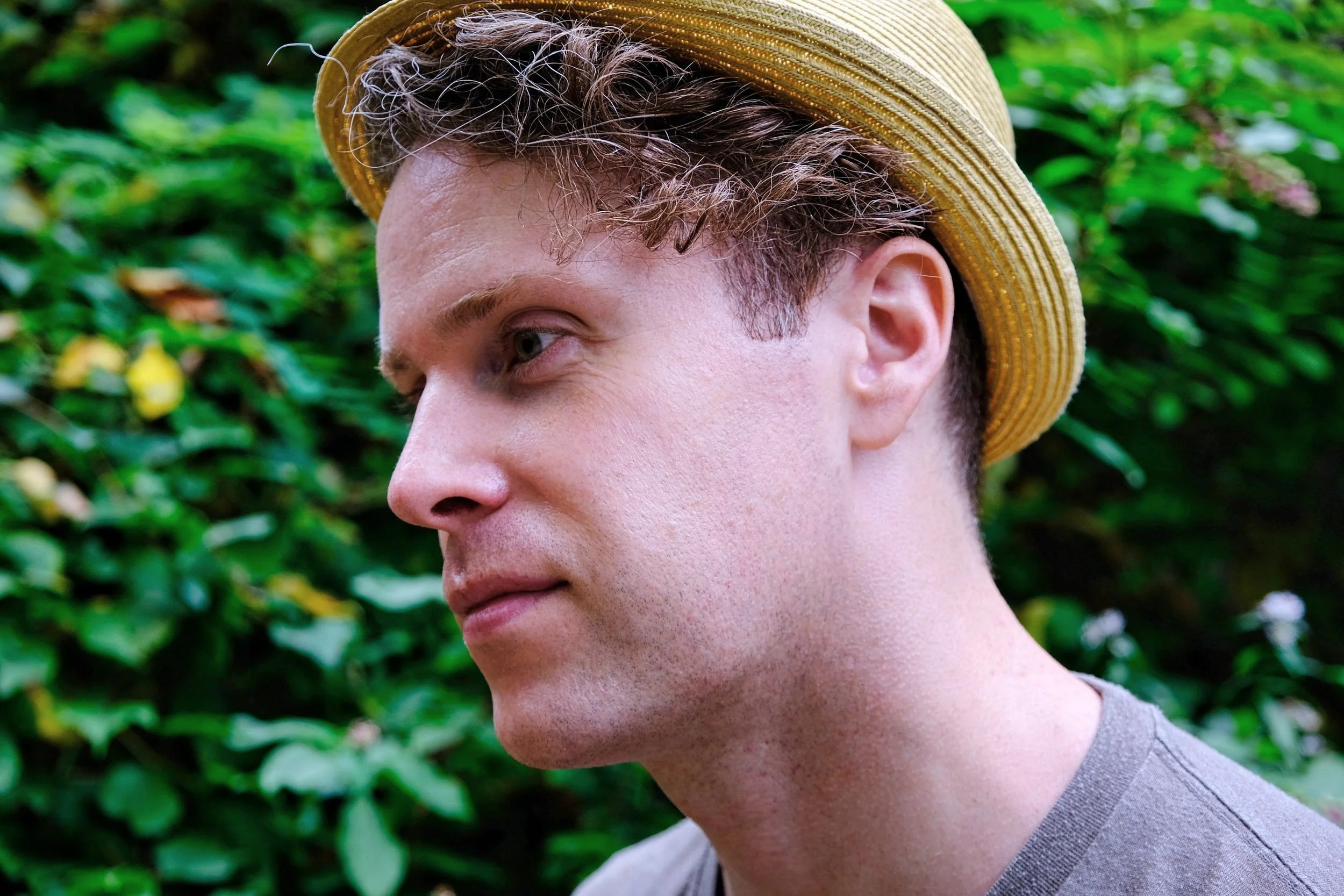 Patrick Shaw, A man wearing a beige straw hat, looking to the left, with a background of green foliage.