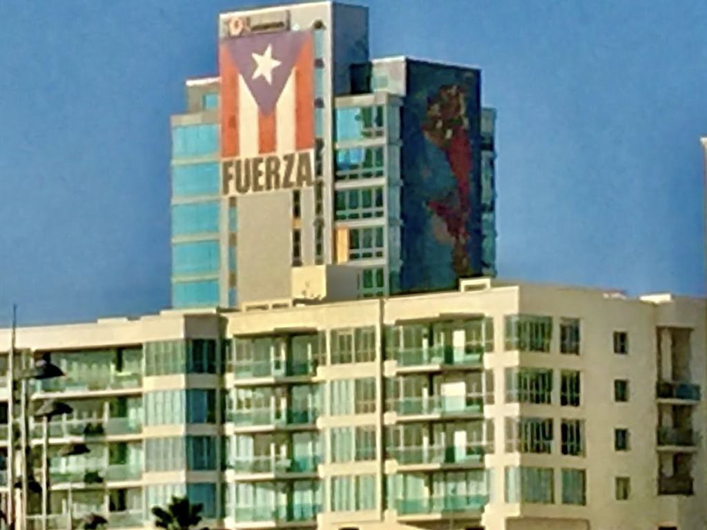An iconic view of a building in San Juan with the Puerto Rican flag and the Spanish word for “strong.” An exhortation and declaration of the enduring strength and resilience of the Puerto Rican people.