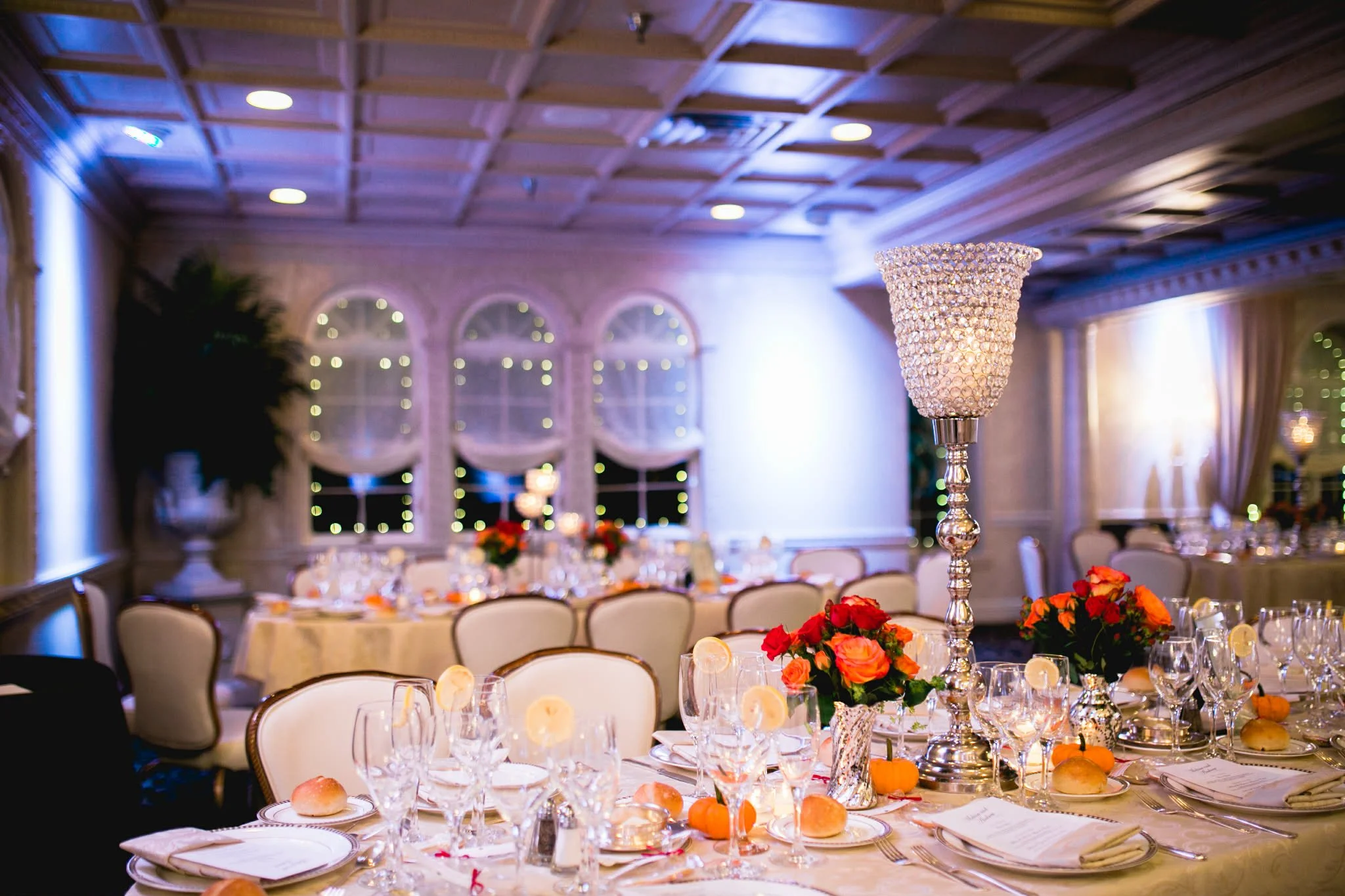 Elegant banquet hall decorated for a formal event with tables set with fine china, glassware, floral centerpieces, and a large crystal chandelier.