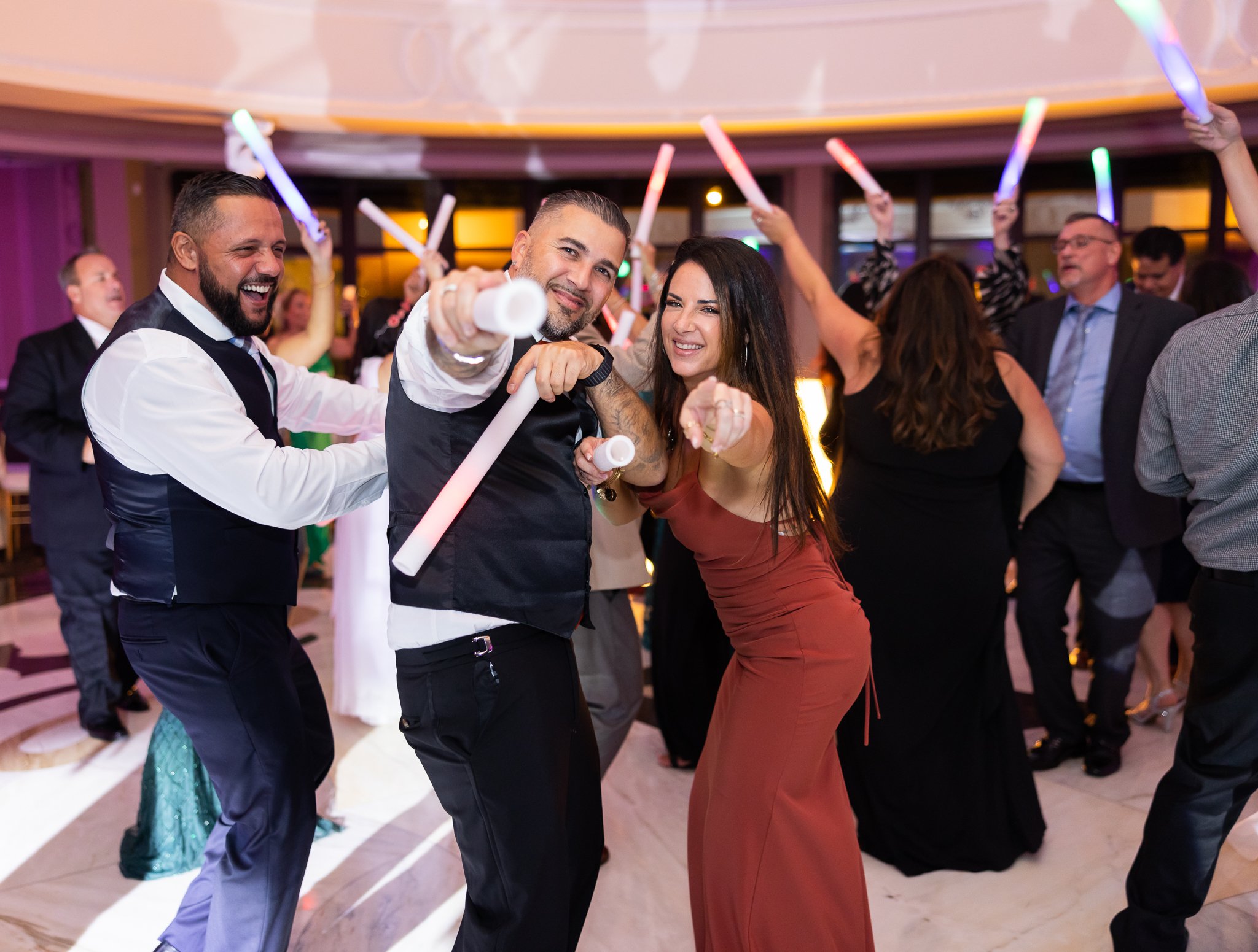 Group of people dancing and celebrating at a party, some holding glow sticks.
