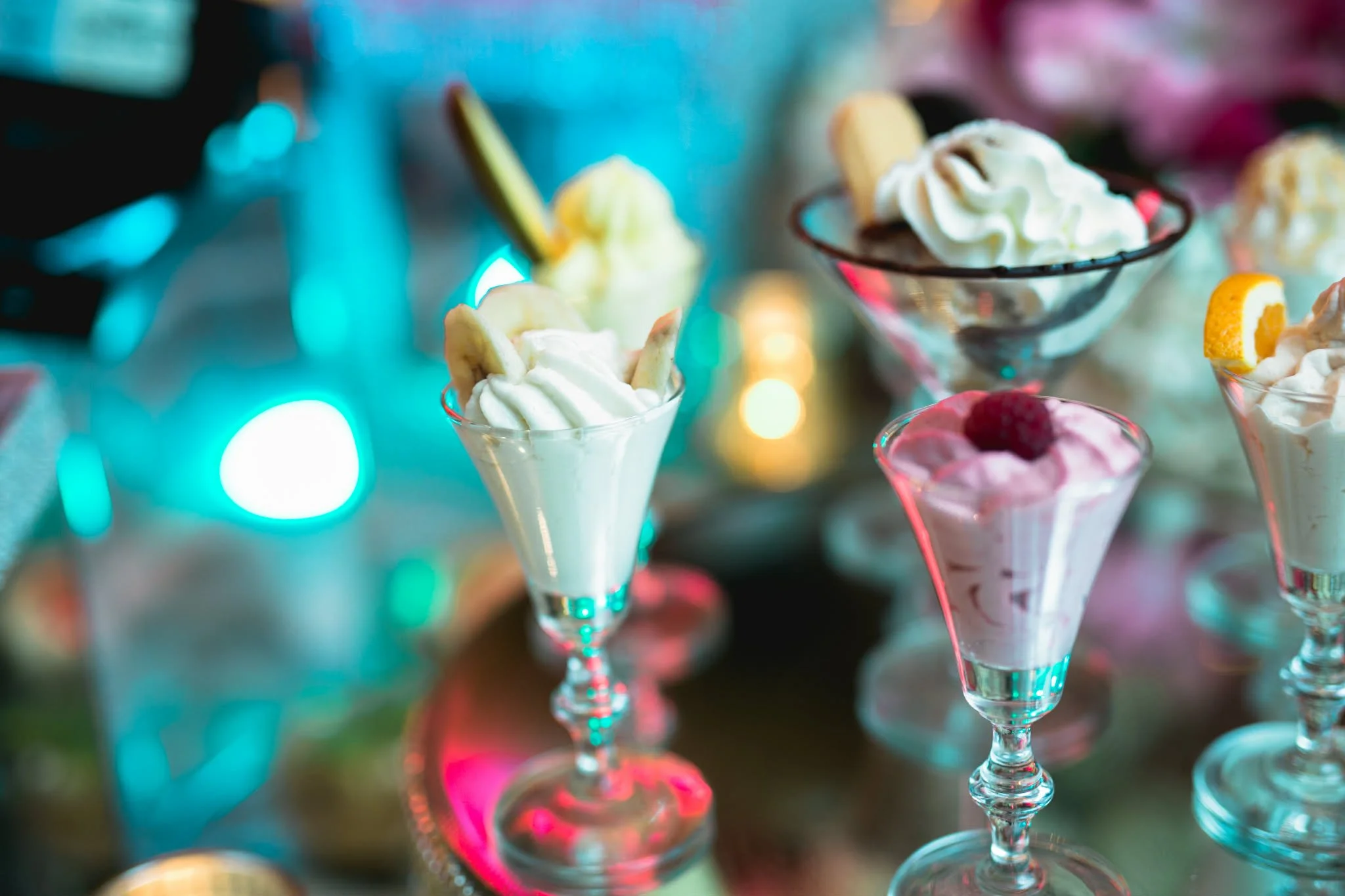 Ice cream sundaes in glass bowls with whipped cream, toppings, and colorful lights in the background.