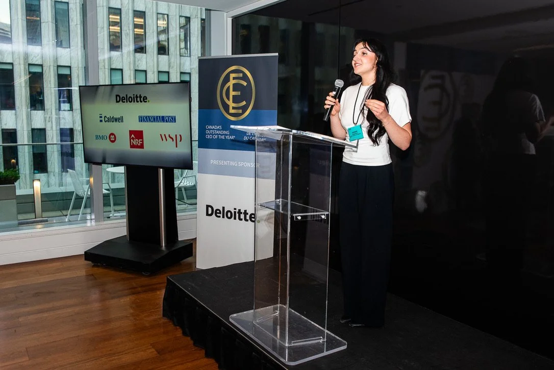 Simone is a white woman with long black hair. She speaks behind a clear podium.