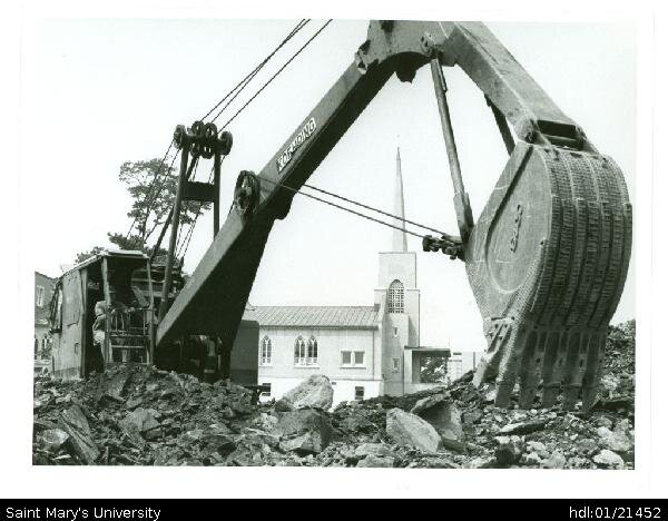  Photograph of excavator breaking the sod (for new high rise residence and academic complex) to the south of old chapel. The upper floor space of the chapel was renovated into the McNally Theatre Auditorium which opened on March 1 1982, with the stag