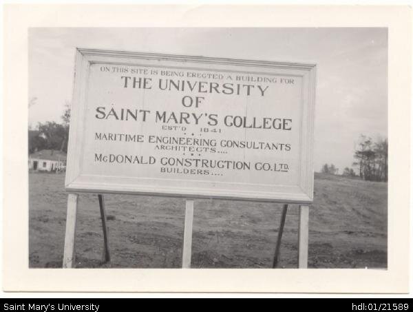  Photograph of the sign (at Inglis and Robie Streets) announcing construction of Saint Mary's University on former Gorsebrook golf course by MacDonald Construction Builders commencing in May 1950. The trees have all been clearcut. Note the cottage or