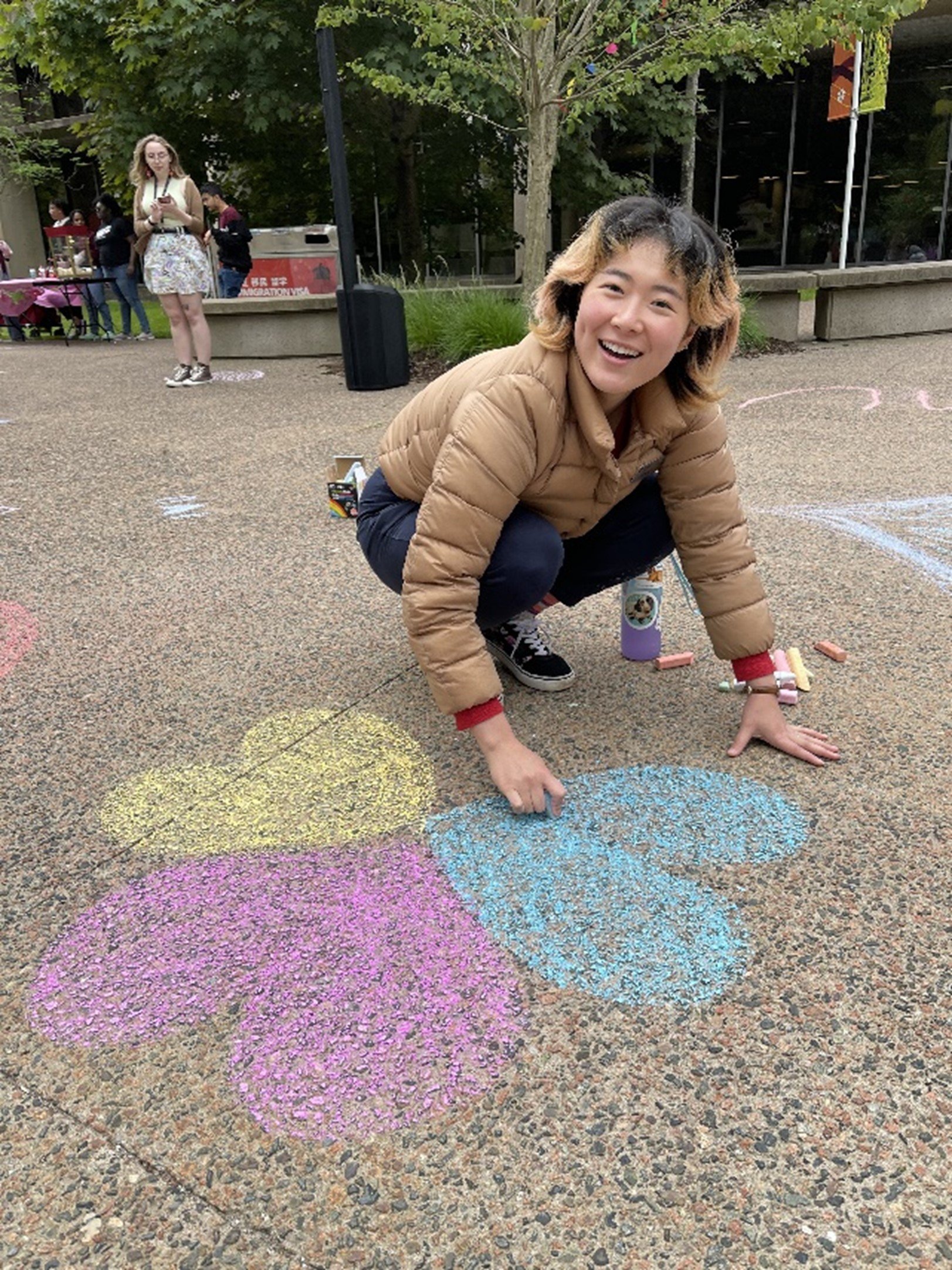  Hanna Sakaki, Alumni Assistant, smiles while making a chalk drawing of different coloured hearts on the Quad pathway. 