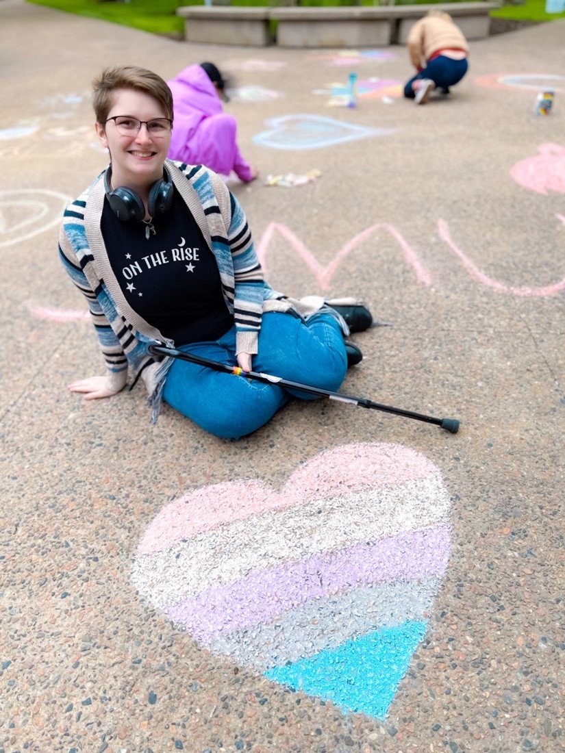  Ken Cornell, SMU student, sits on the Quad pathway next to a chalk heart drawn in genderfluid pride colours.  