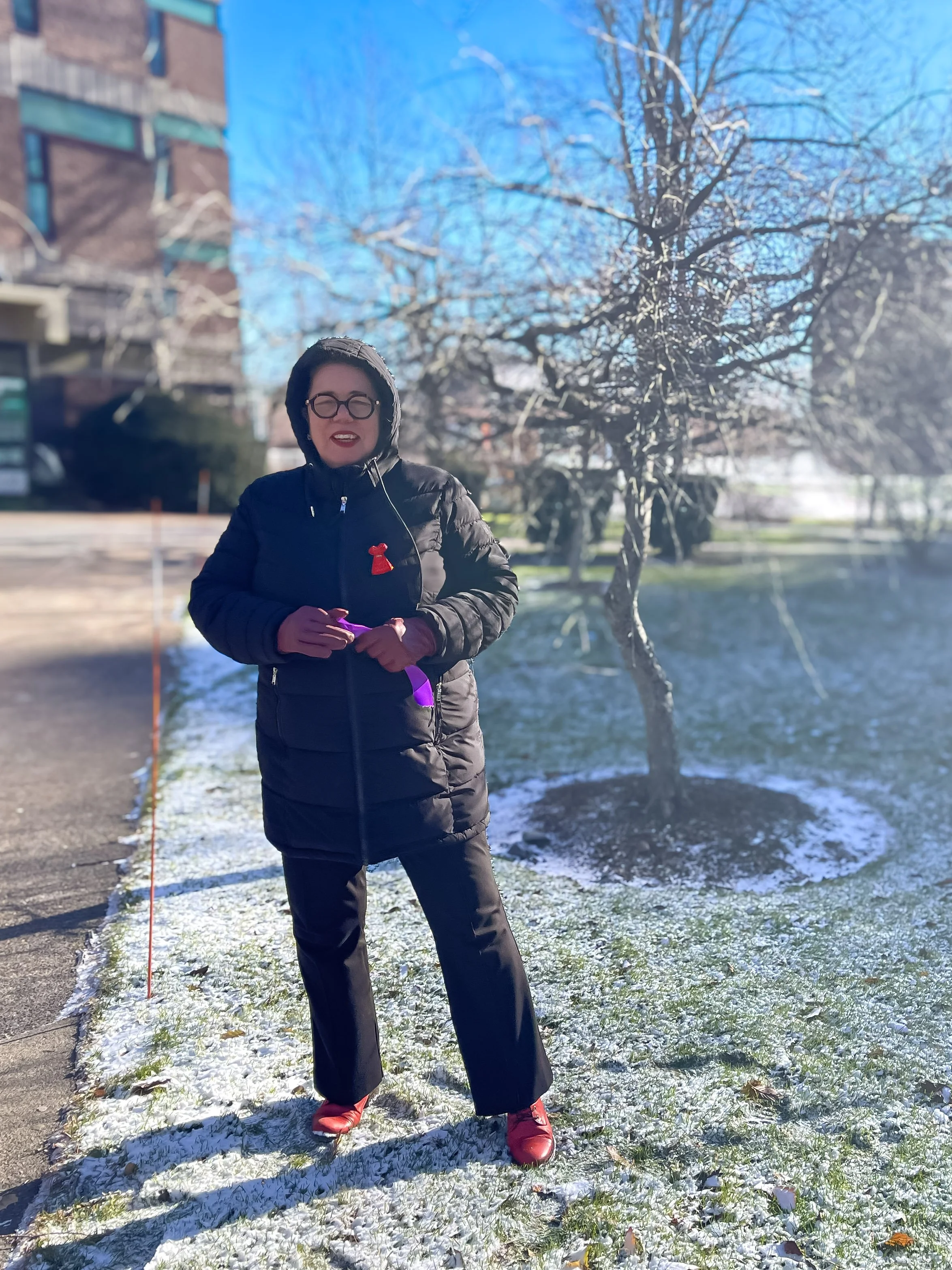 Dr. Dea stands outside and holds a purple ribbon