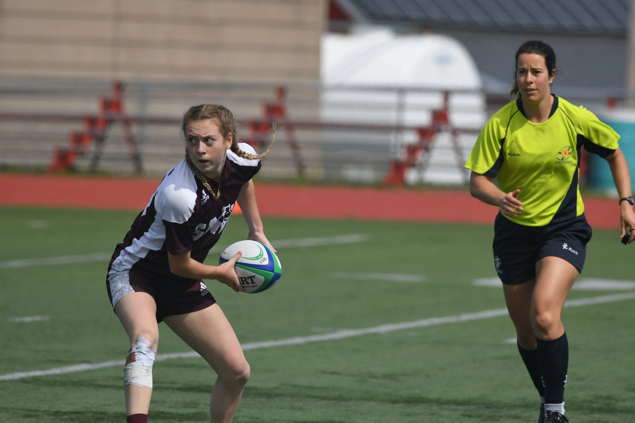 Julie holds the ball on the rugby pitch as an opponent runs toward her