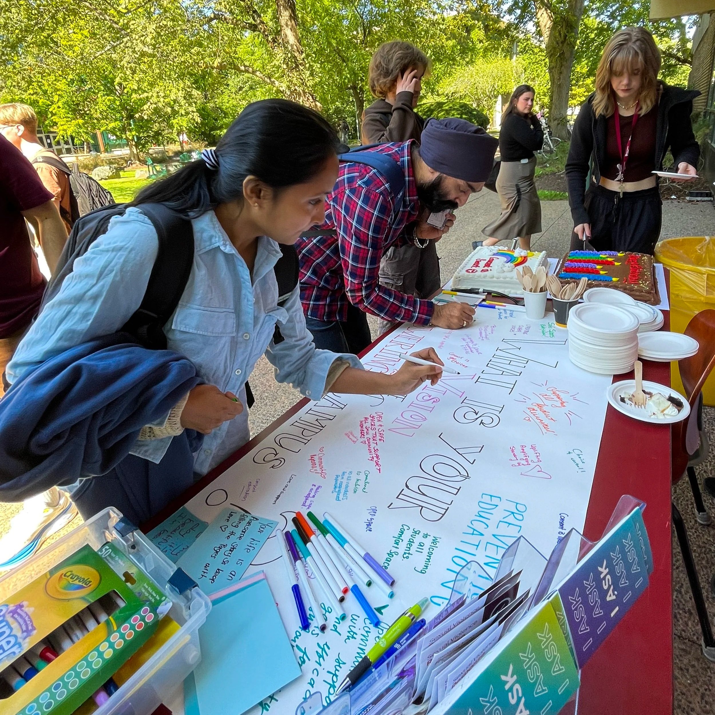 Students write their answers for 'what is your vision for campus' on a large white banner