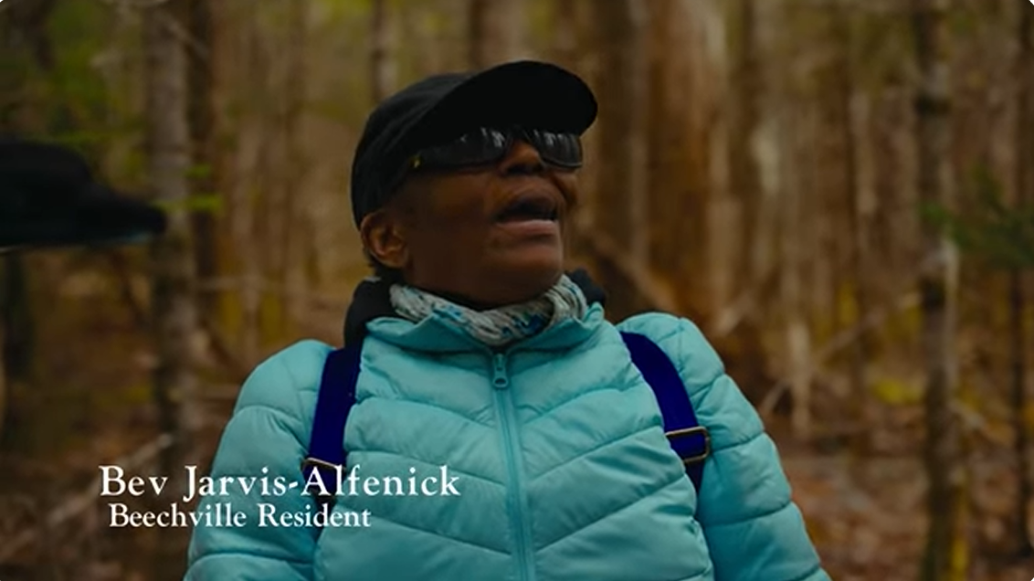 Bev speaks to the camera in the woods