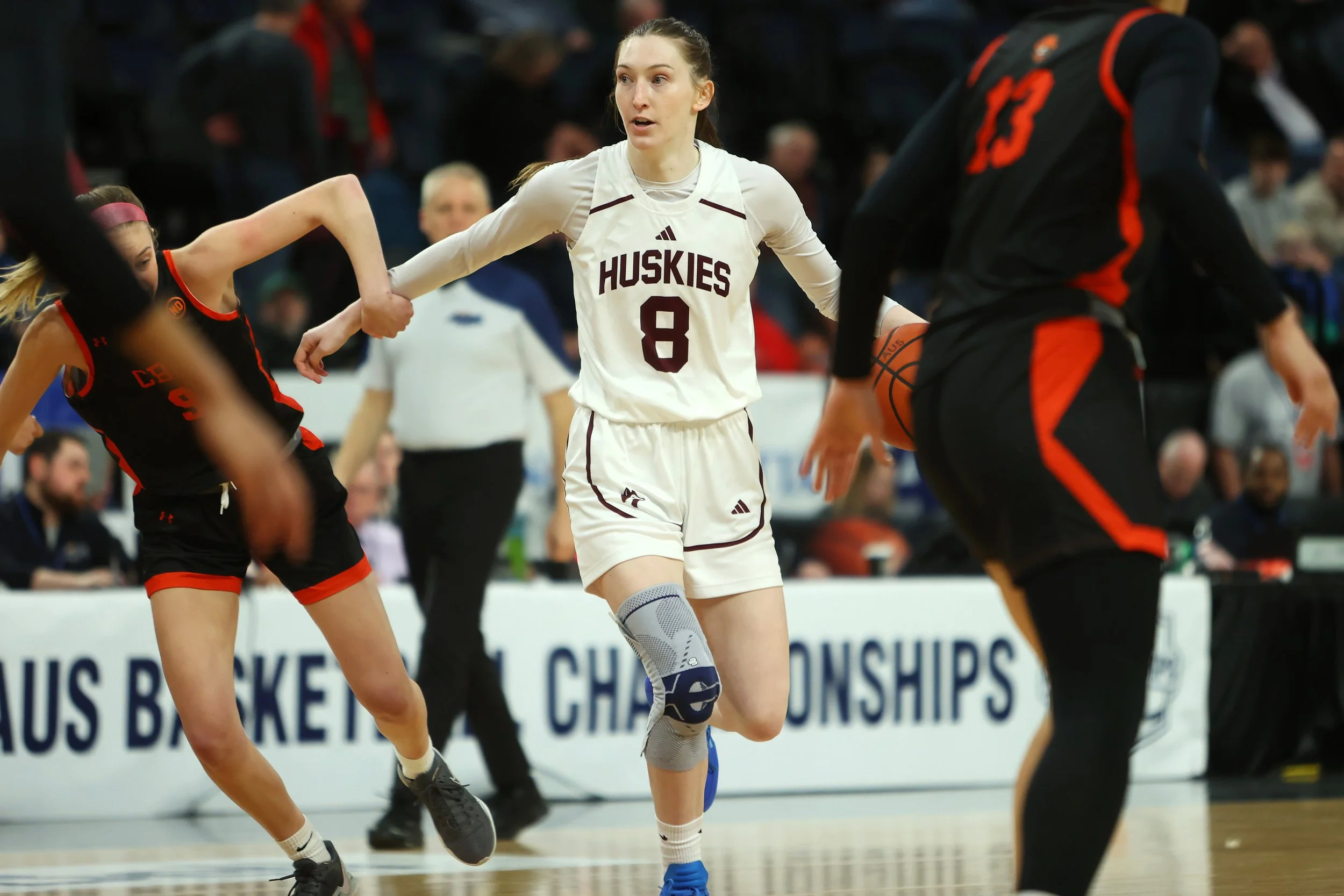 Clara plays basketball on court wearing a white Huskies jersey