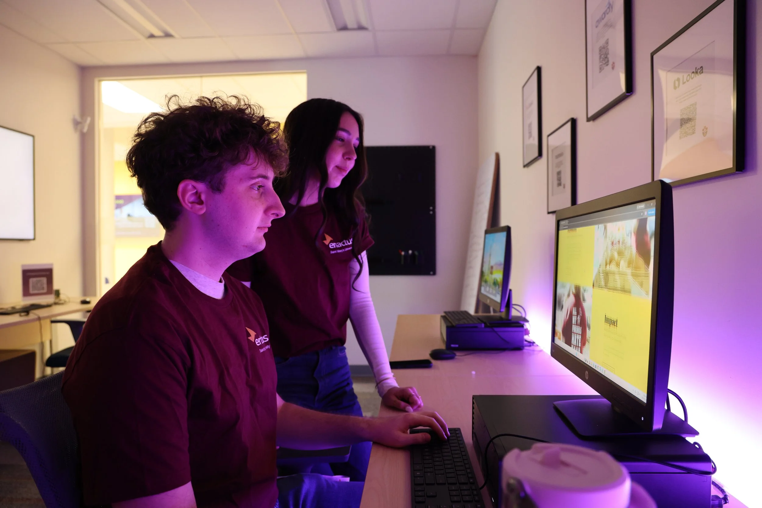 nathan and Leah wear Enactus tshirts and look at a computer screen together