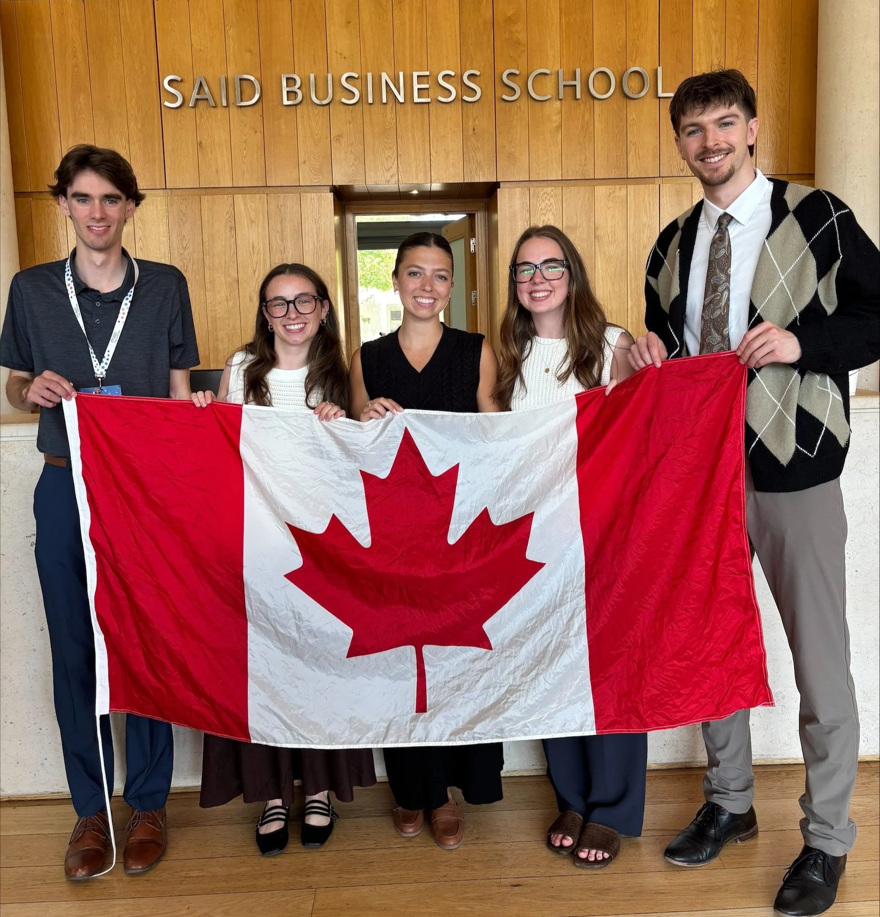 The team holds a large Canadian flag under a sign reading Said Business School