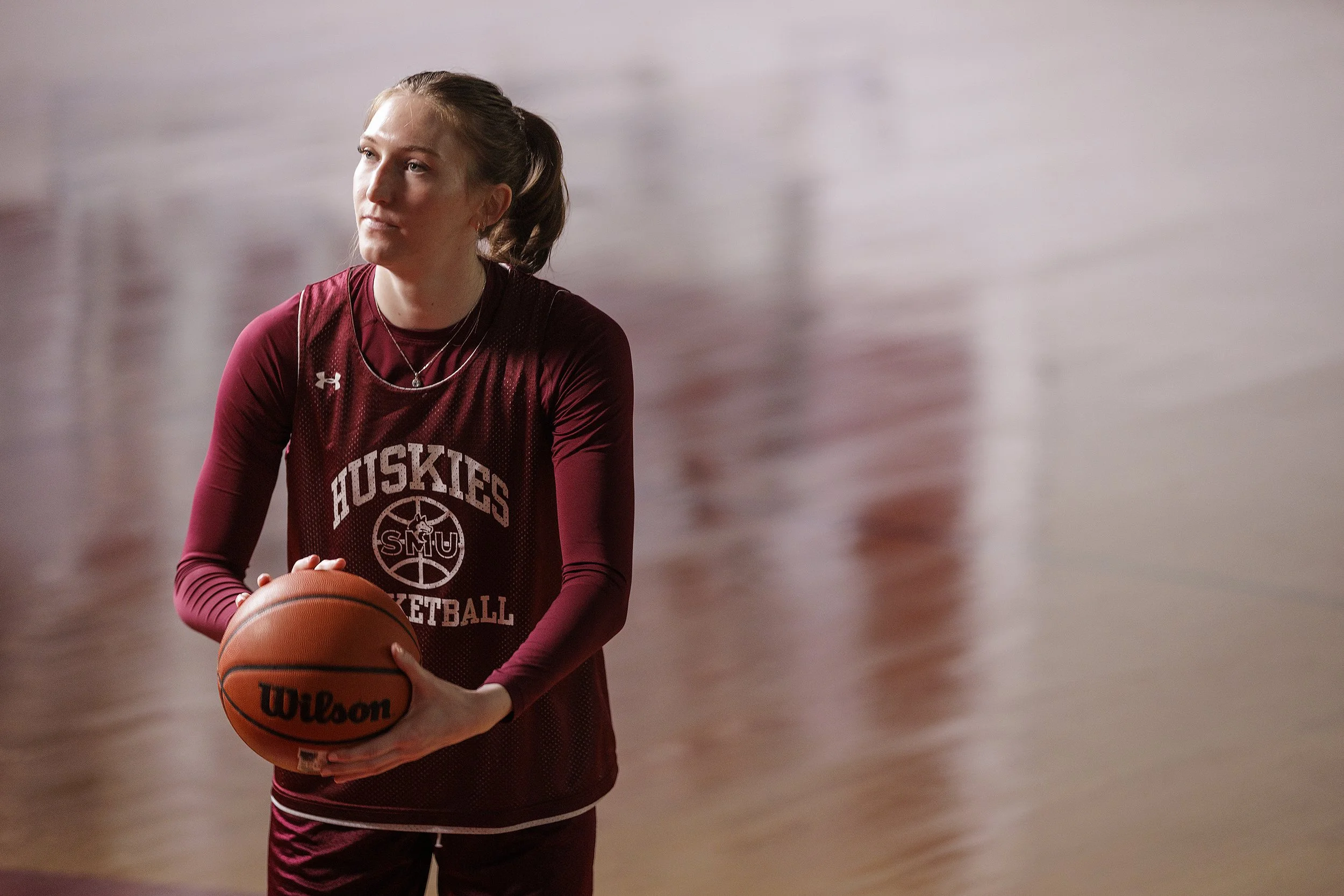 Clara practices basketball on court wearing a maroon Huskies jersey