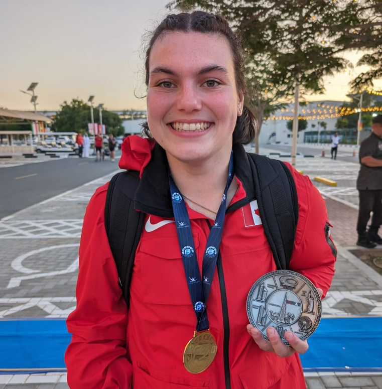 Katie, a white woman with brown hair, wears a medal and a red Canada jacket