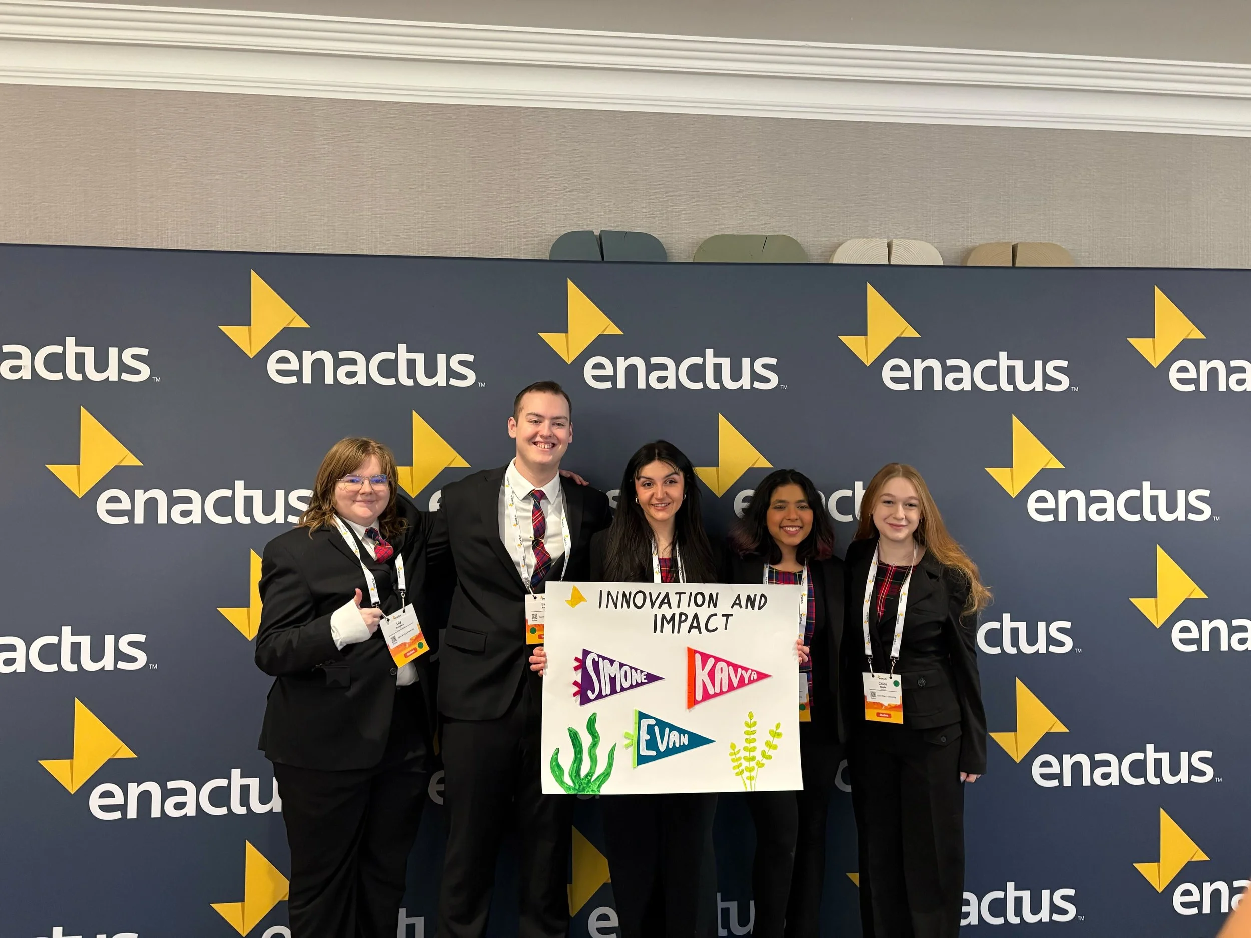 Five team members hold a sign reading Innovation and Impact