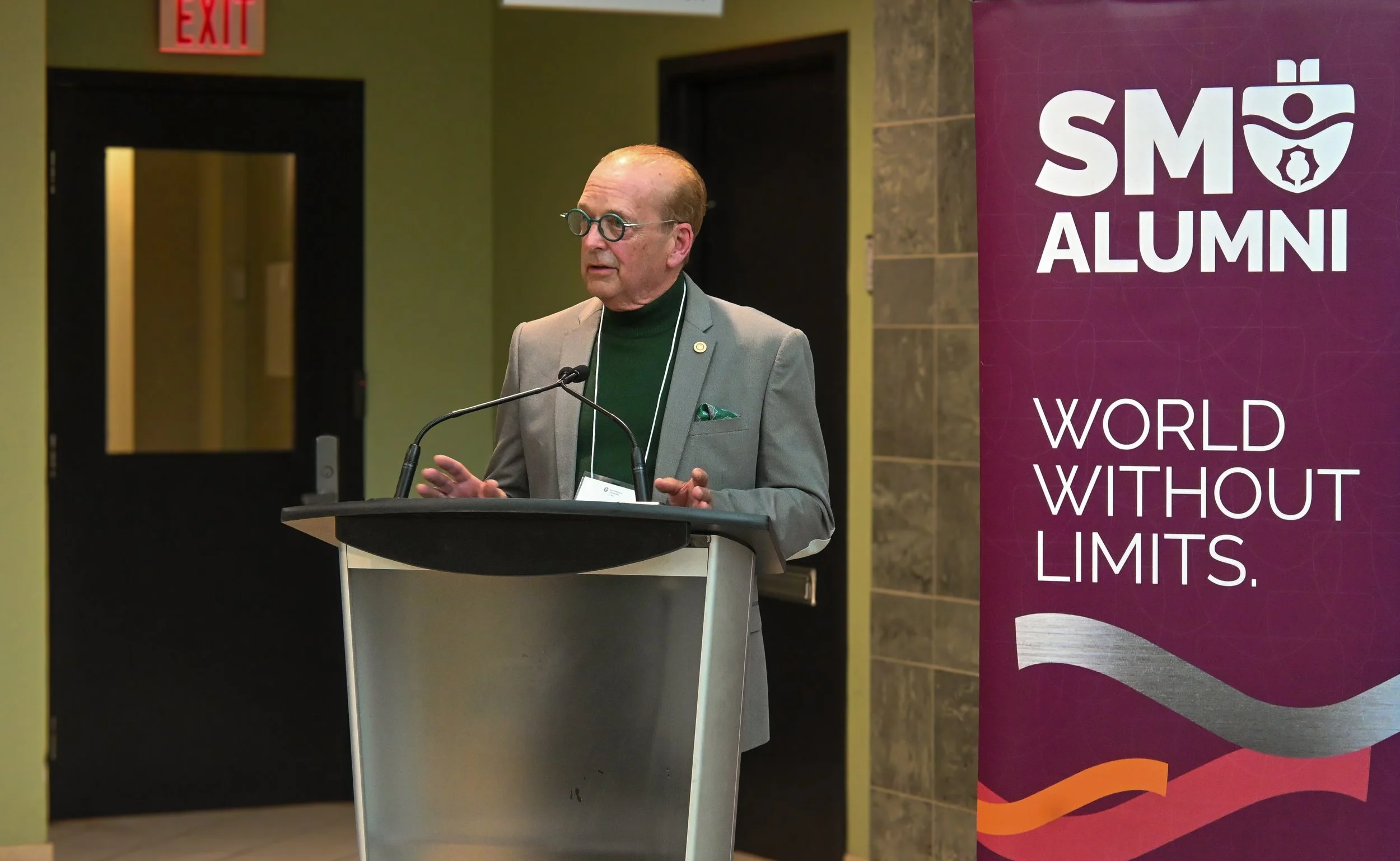 William speaks at a podium next to a SMU alumni banner