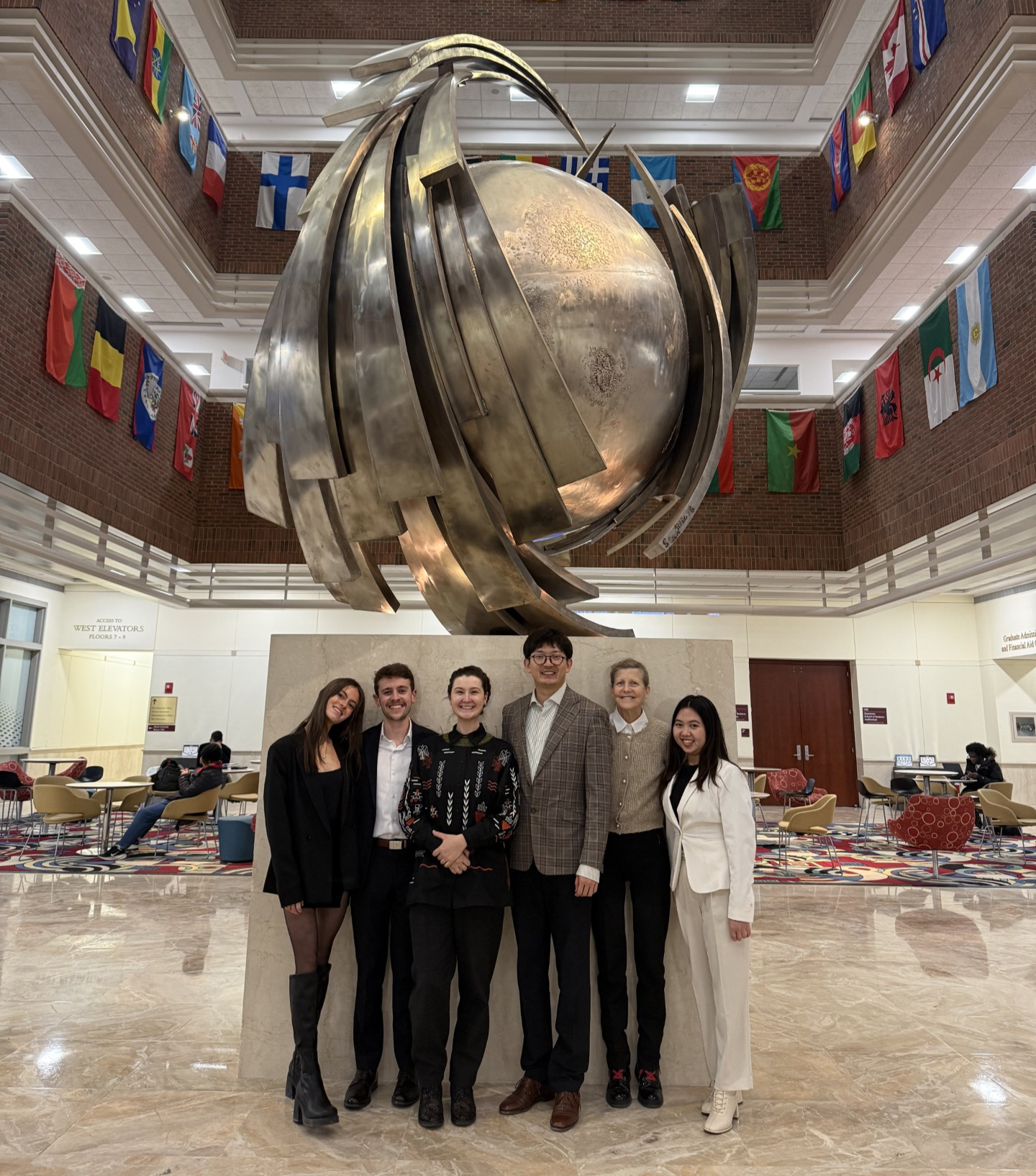 The student team poses together in front of a large metal sculpture