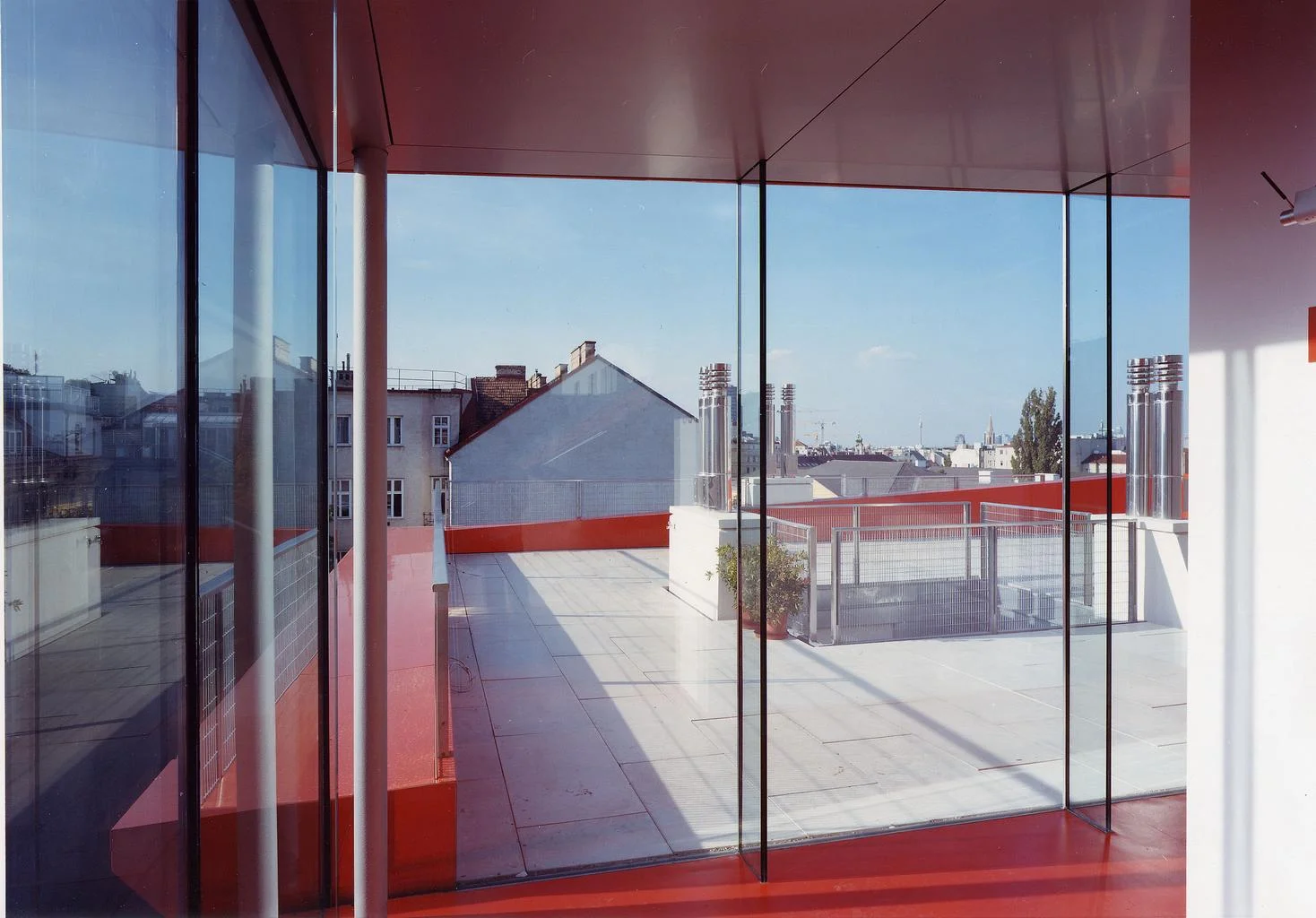 …der zugang auf die terrasse erfolgt über den wintergarten aus einer nurglaskonstruktion – glasschwerter und zarte stahlstützen tragen die fassade und das dach, der orange kautschukboden spiegelt sich in der aluminiumdecke und erzeugt ein warmes sommerliches ambiente auch im winter…