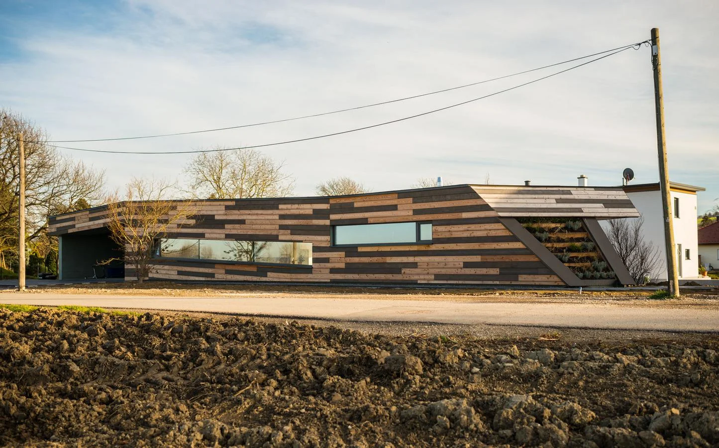 das einfamilienhaus in freundorf bei tulln ist sowohl ein städtebaulicher beitrag zum bauen am ortsrand, als auch ein beitrag zum individuell geplanten fertigteilhausbau. die lage des grundstücks am ortsrand, umgeben von einerseits standardisierten fertigteilhäusern, die mit ihrer umgebung nicht korrespondieren und feldern, über die der nordwestwind frei auf den bauplatz trifft, fordert ein spezielles statement. 