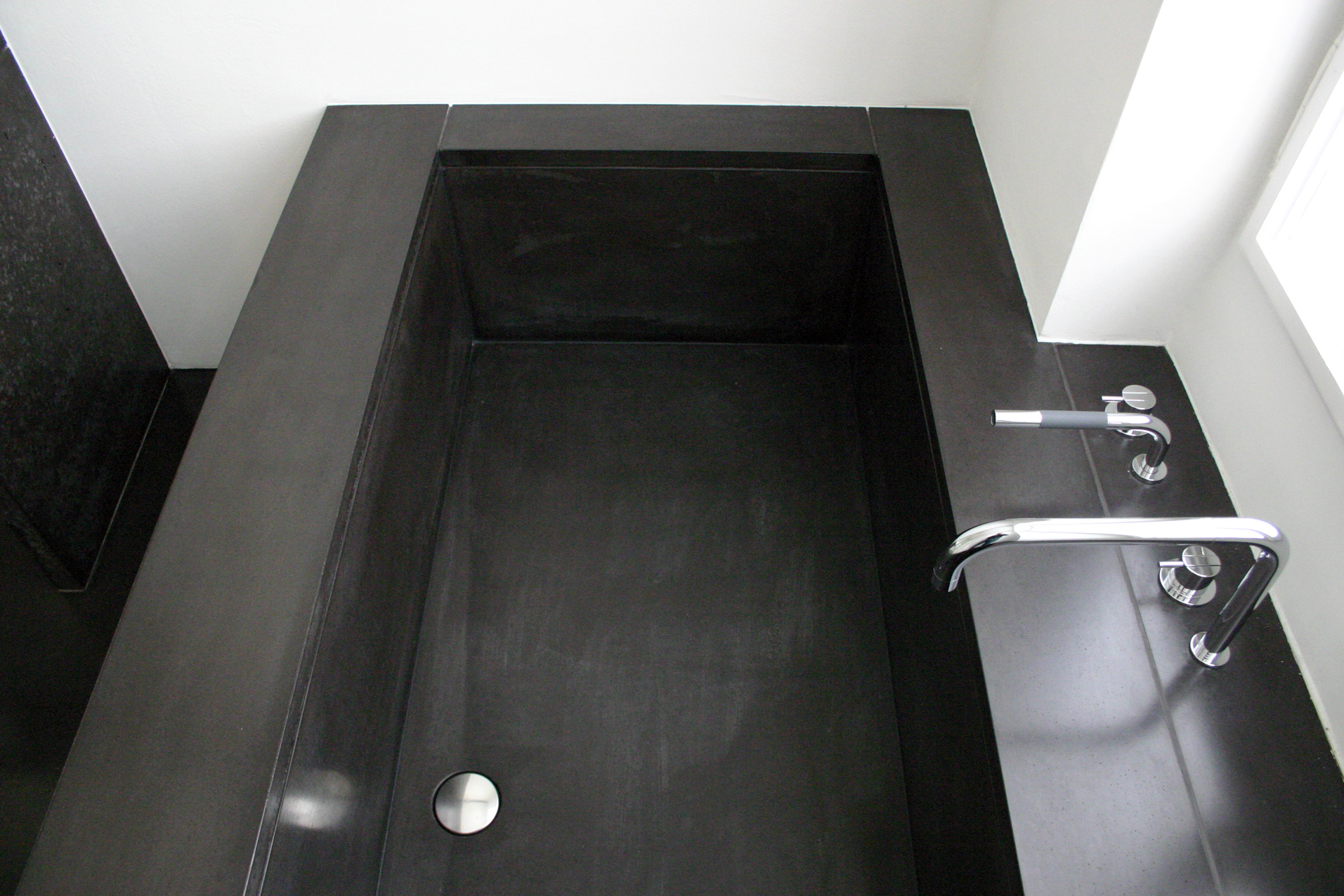  einbau eines badezimmers mit wanne und großzügiger dusche in ein klassisches kabinet einer altbauwohnung. schwarzer beton am boden, im gefälle verlegt in der dusche und als verkleidung der badewanne innen und aussen. 