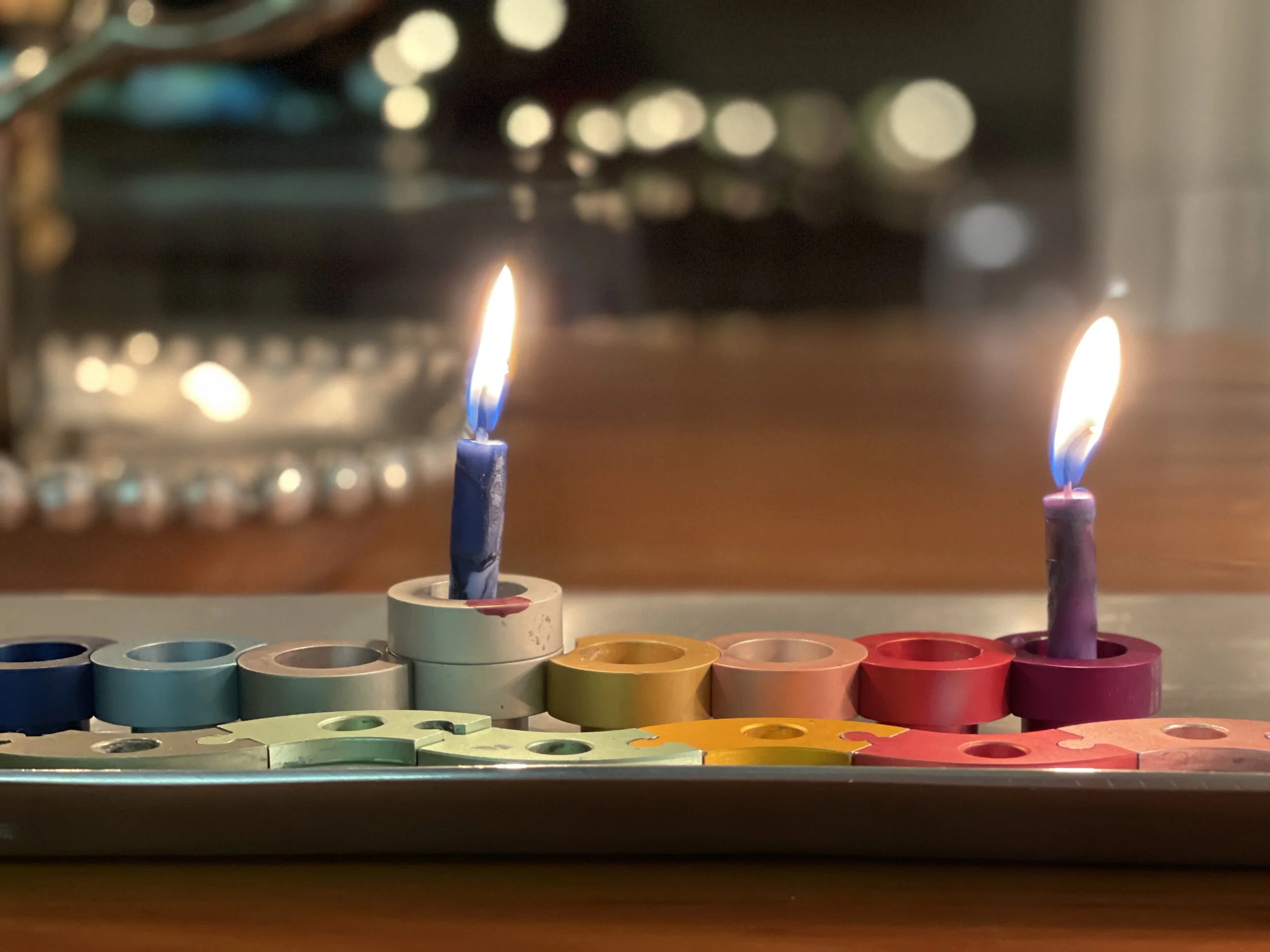 Two lit birthday candles on a table with circular colored wax melts.