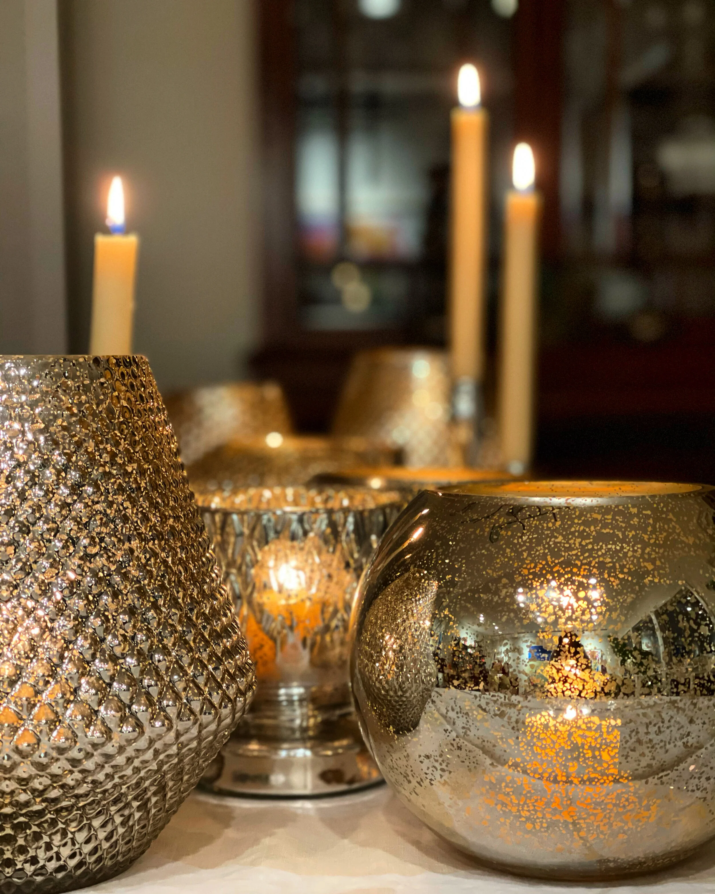 Close-up of decorative metallic candle holders with candles and a glass container in the background.